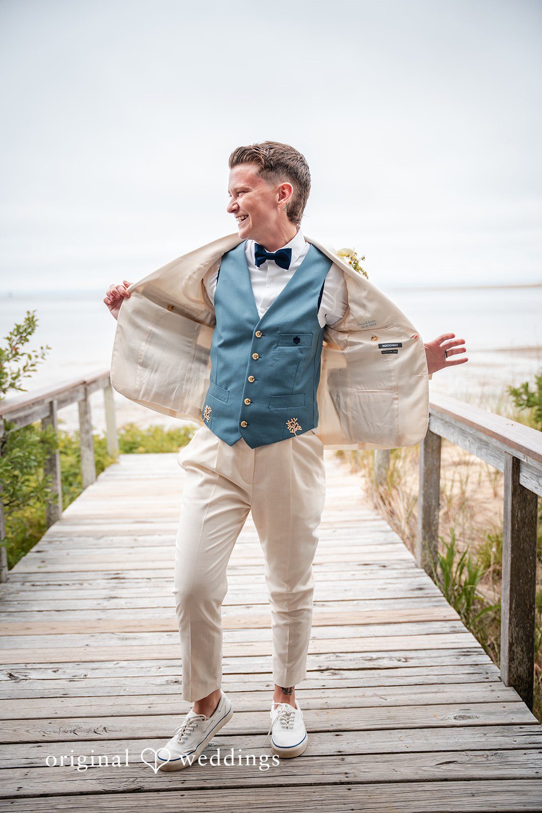 Jacqueline + Sarah A groom playfully throwing his arms wide while walking along a wooden boardwalk.