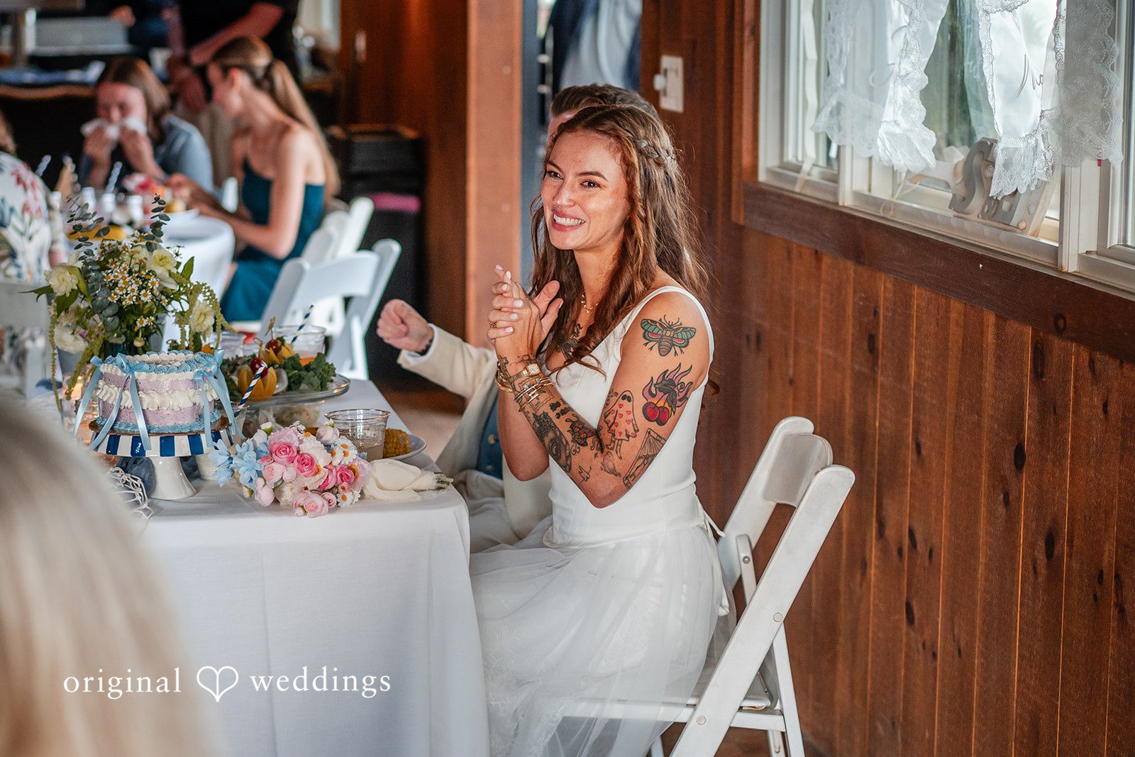 Jacqueline + Sarah A guest sitting at a wooden reception table during a wedding celebration.