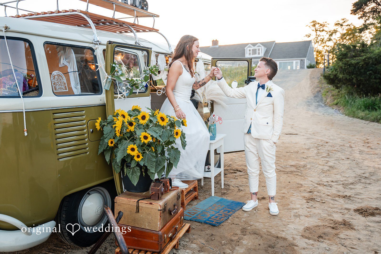 Jacqueline + Sarah A couple standing outside a green vintage van decorated with sunflowers.