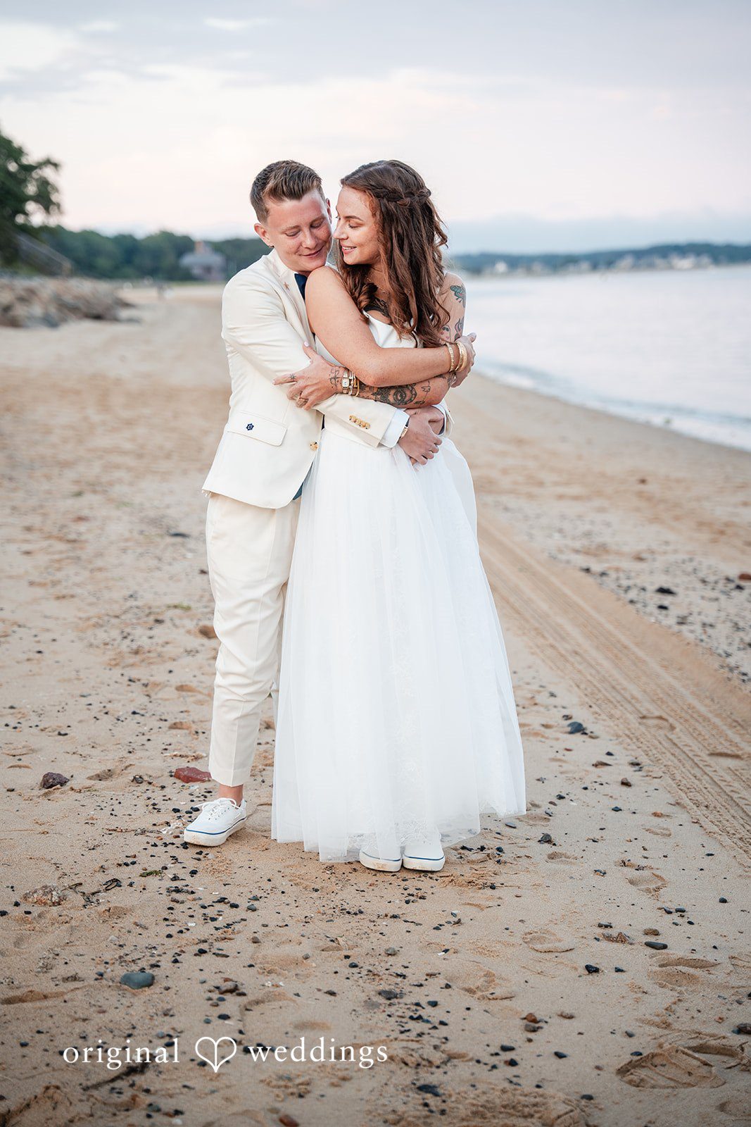 Jacqueline + Sarah A groom dipping his bride backward for a romantic pose on a sandy beach.