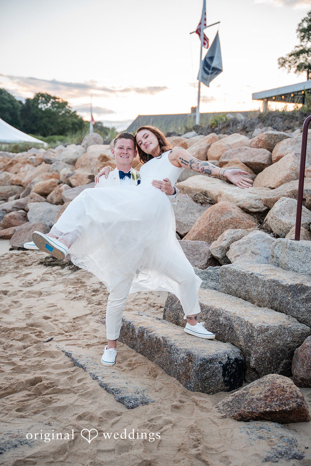 Jacqueline + Sarah A groom playfully balancing on a rocky walkway near the water.