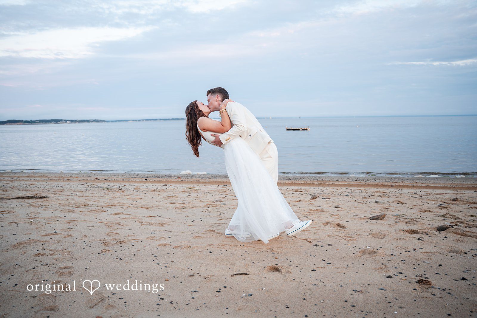 Jacqueline + Sarah A bride and groom kissing on an empty sandy beach at dusk.