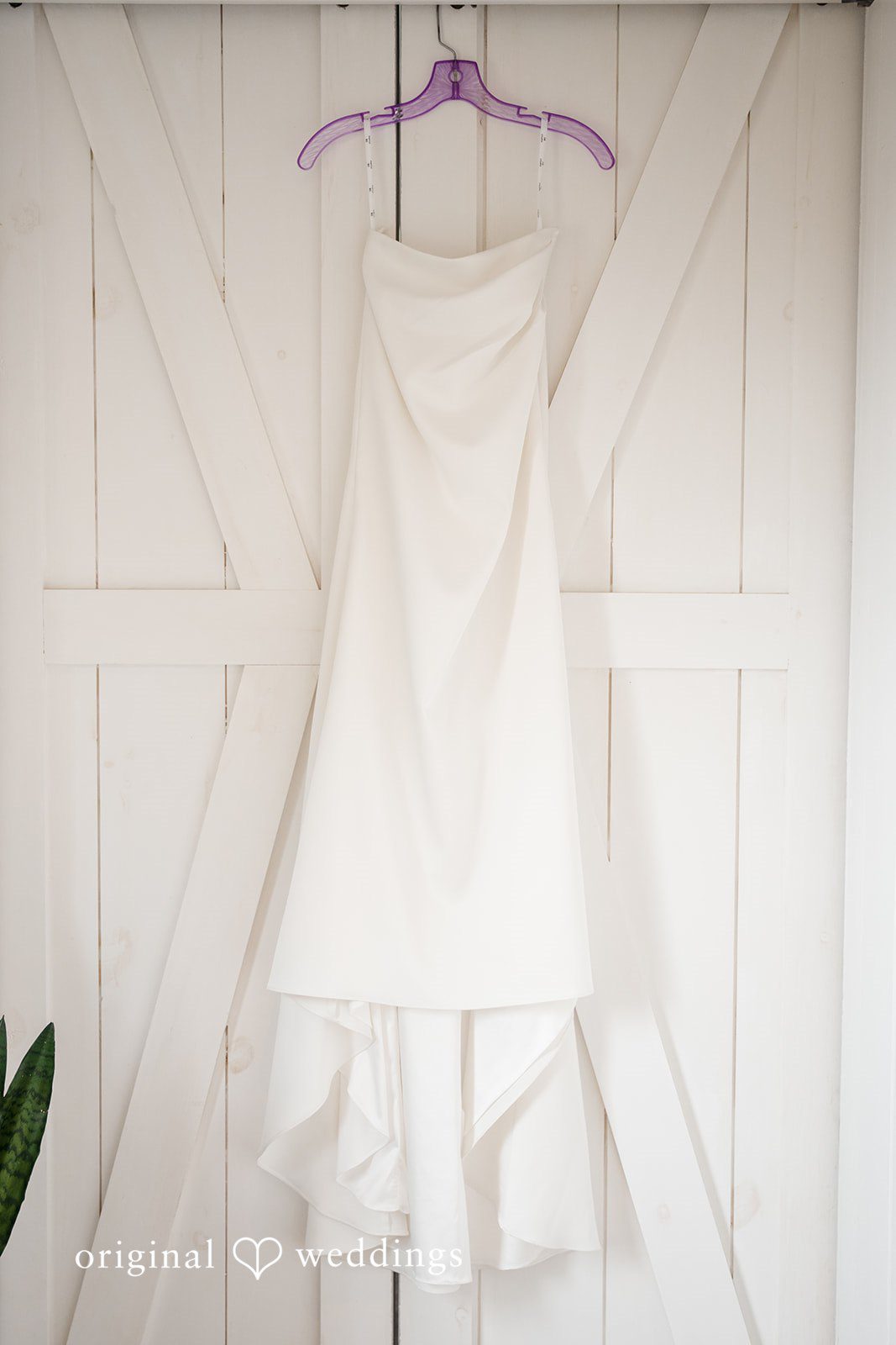 Jacqueline + Sarah A white wedding dress hanging against a light-colored wooden door.