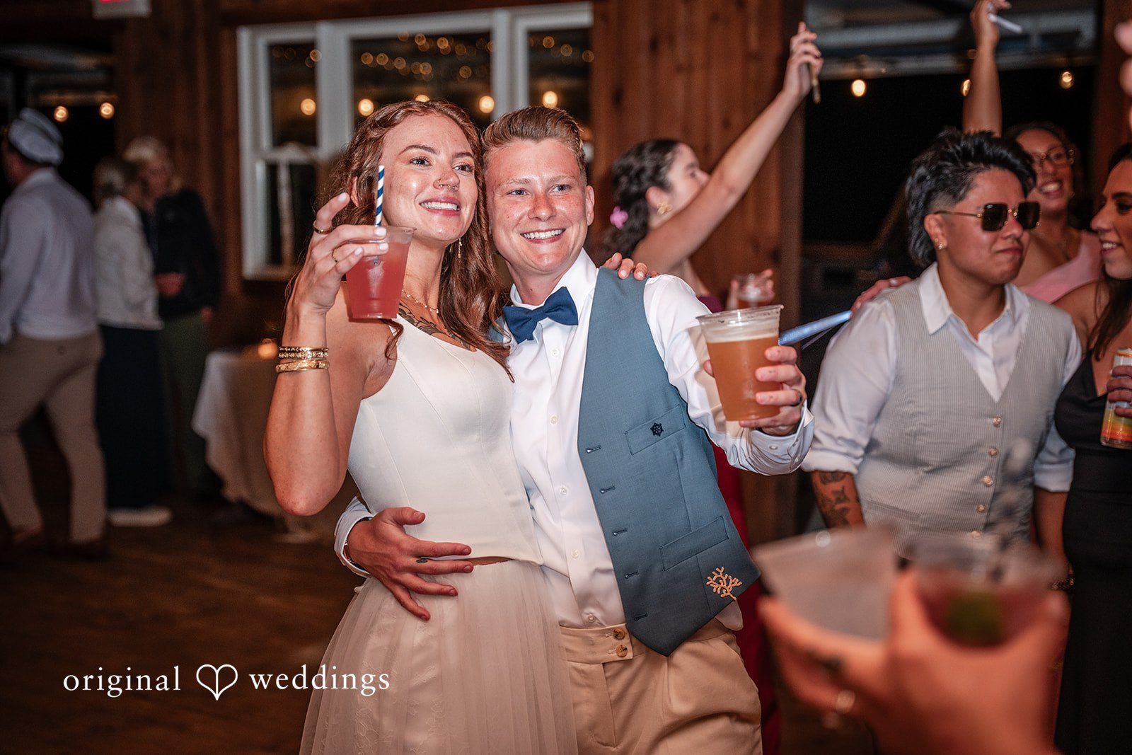 Jacqueline + Sarah A bride and groom holding drinks and smiling together while dancing with guests during their wedding reception.