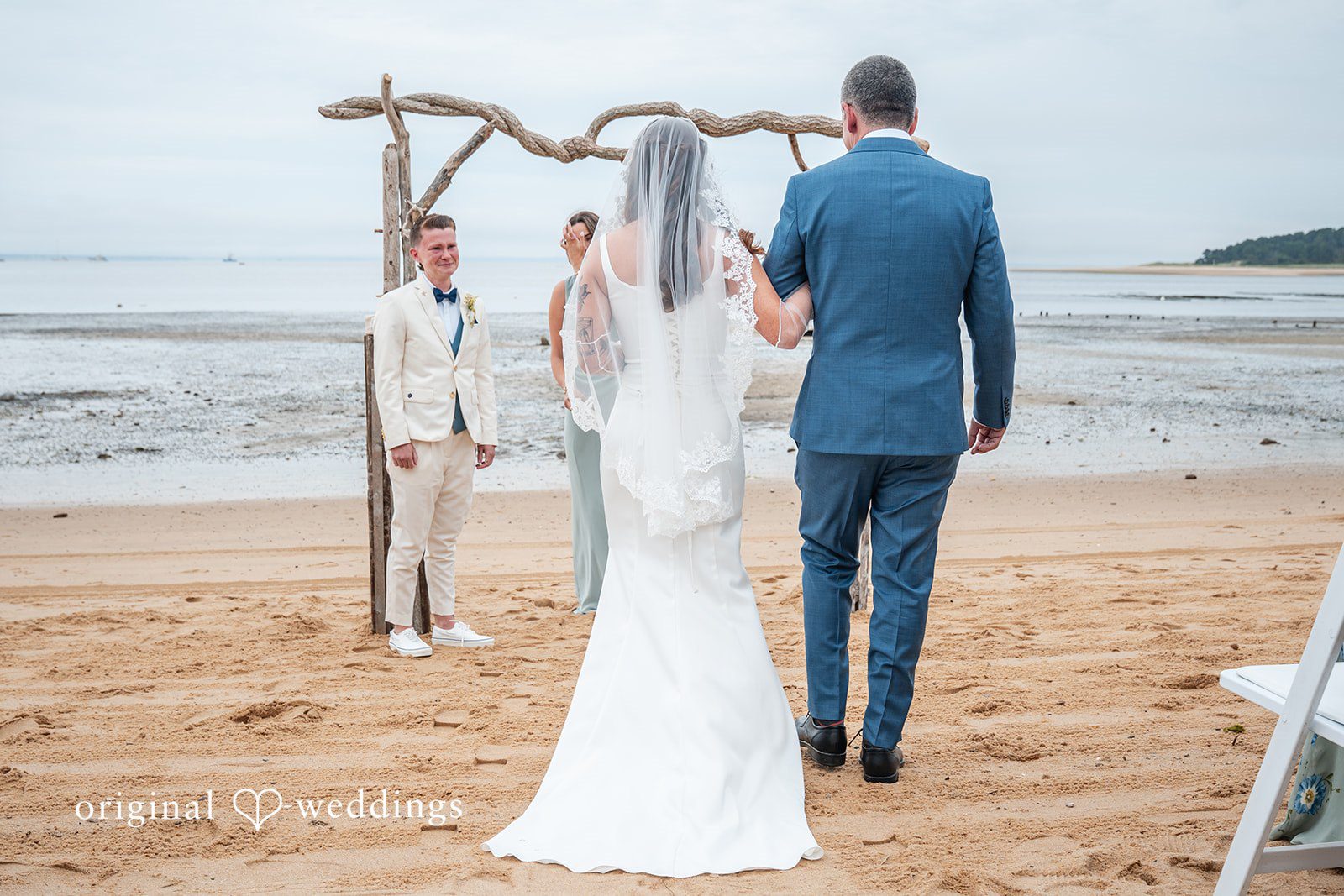 Jacqueline + Sarah A rear view of a bride walking together along a sandy beach.