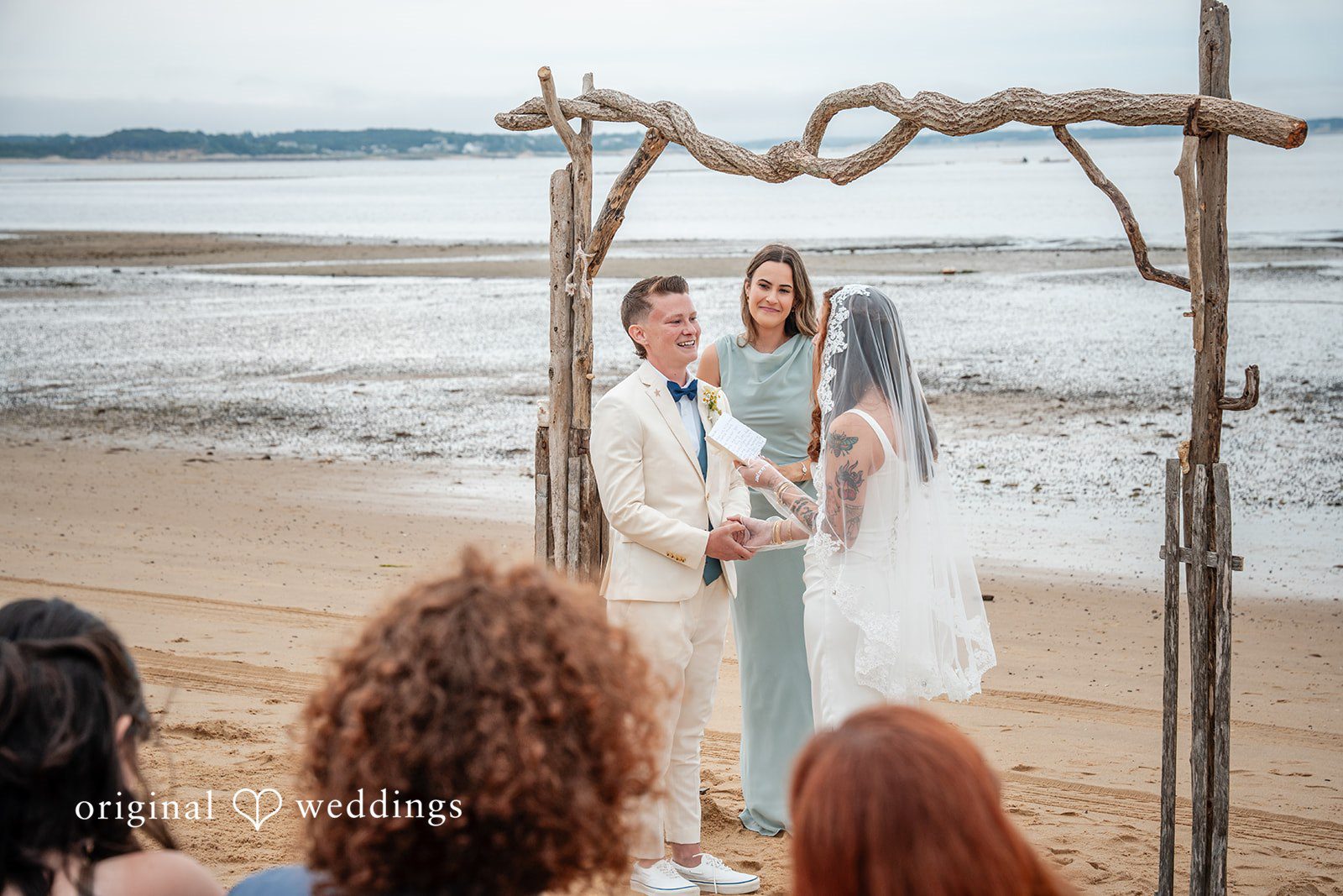 Jacqueline + Sarah A couple standing under a wooden arch during their wedding ceremony.
