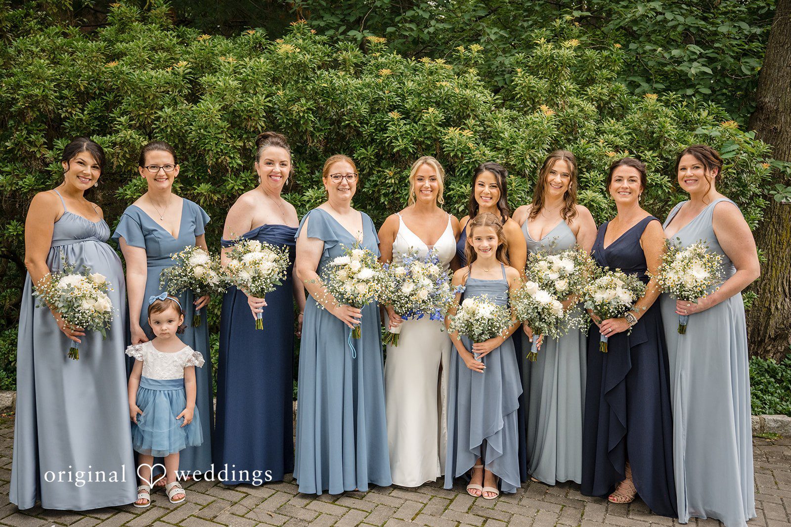 Morgan + Colin A large bridal party wearing shades of dusty blue posing together.
