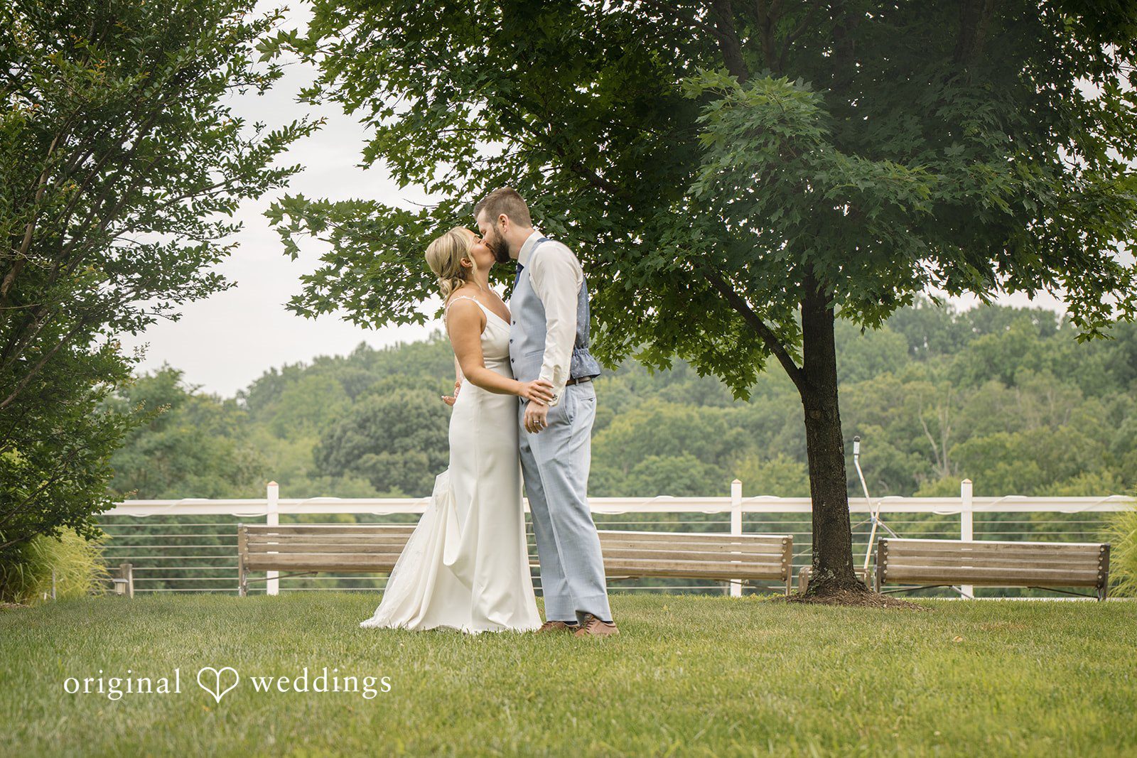 Morgan + Colin A bride and groom embracing on a grassy lawn with a white fence behind them.