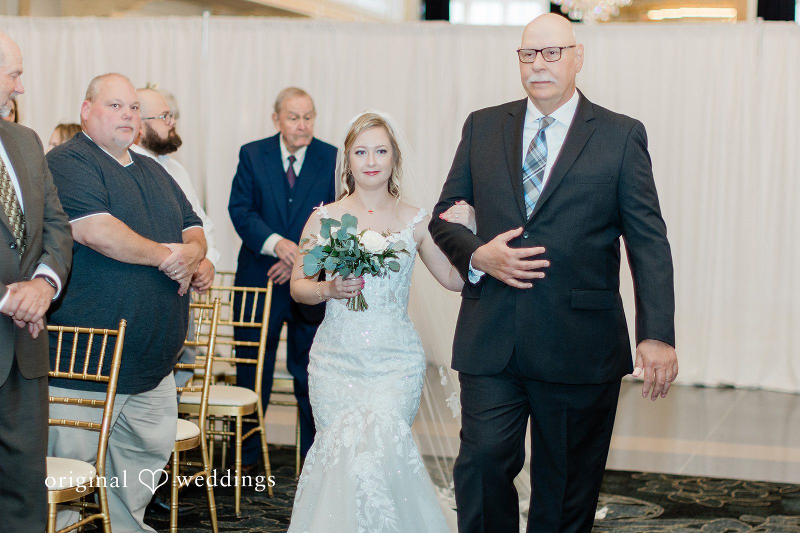 Sara + Michael A bride walking down the aisle linked arms with an older man in a suit.