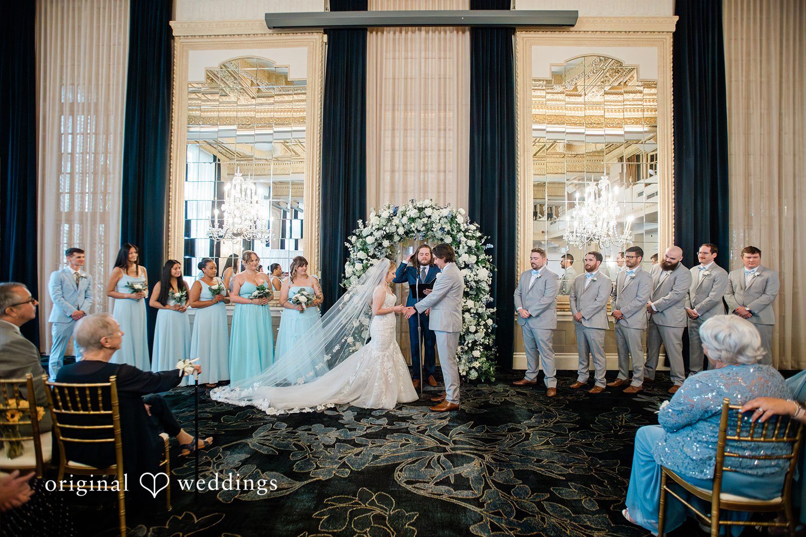 Sara + Michael A wedding party gathered around the altar under grand columns during a ceremony.
