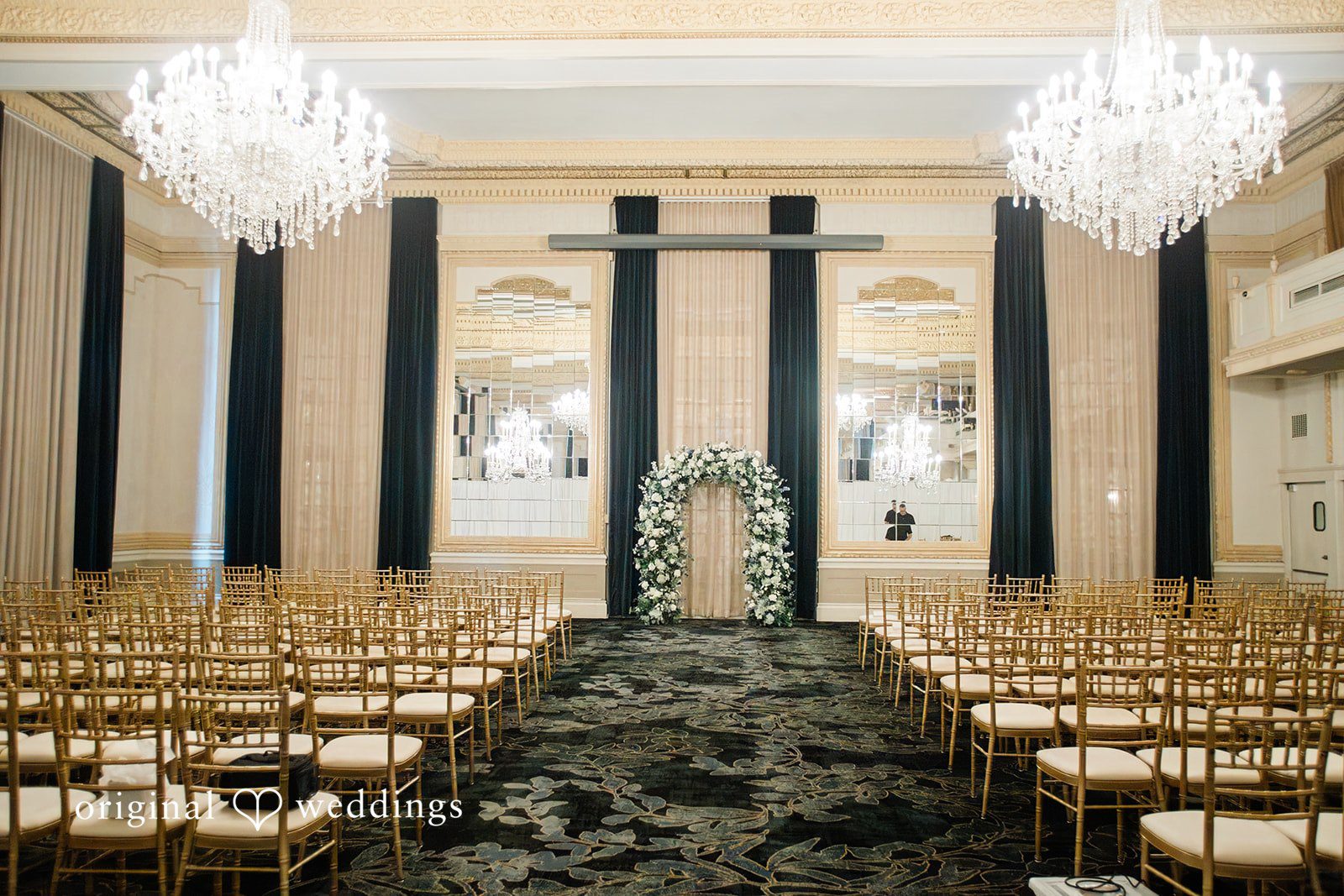 Sara + Michael An empty wedding ceremony aisle lined with chairs leading to a grand altar with pillars.