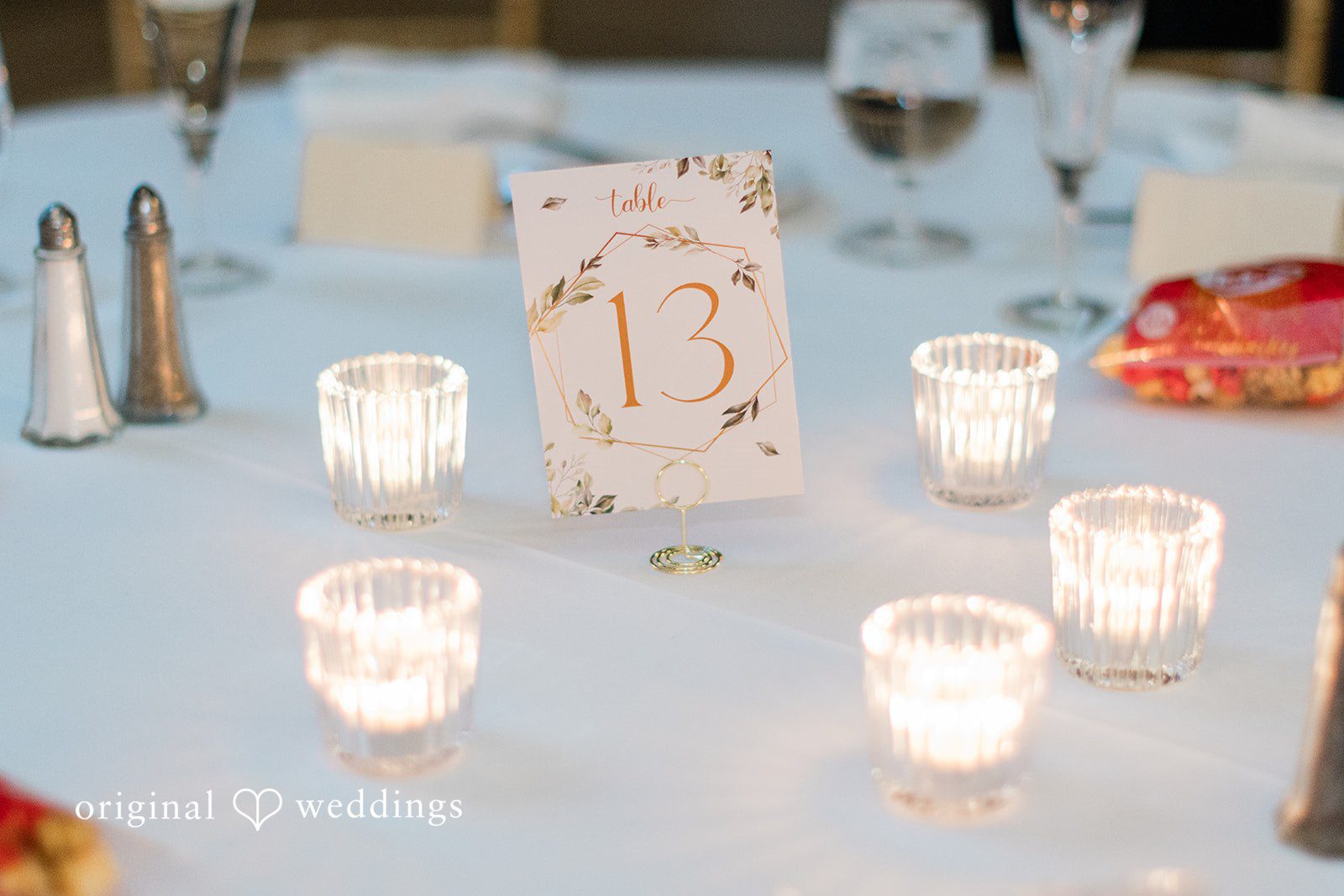 Sara + Michael A close-up of small glowing votive candles and a table number on a reception table.