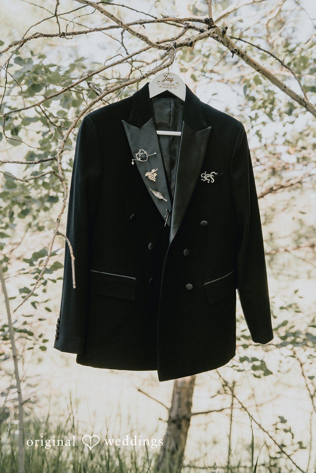 Jennifer + Danielle A black wedding tuxedo jacket hangs from a tree branch.