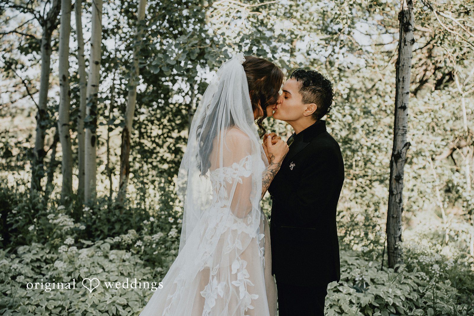 Jennifer + Danielle A Couple share a close embrace in a wooded setting.