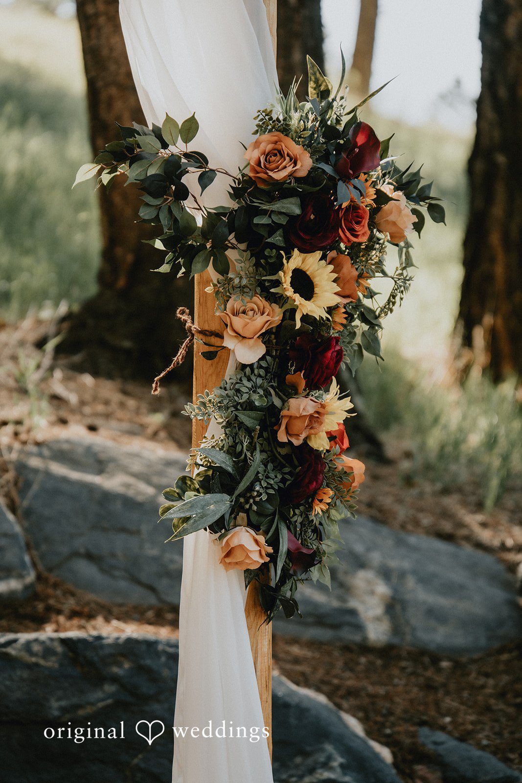Jennifer + Danielle A floral wedding arrangement with sunflowers sits on a white fabric runner.