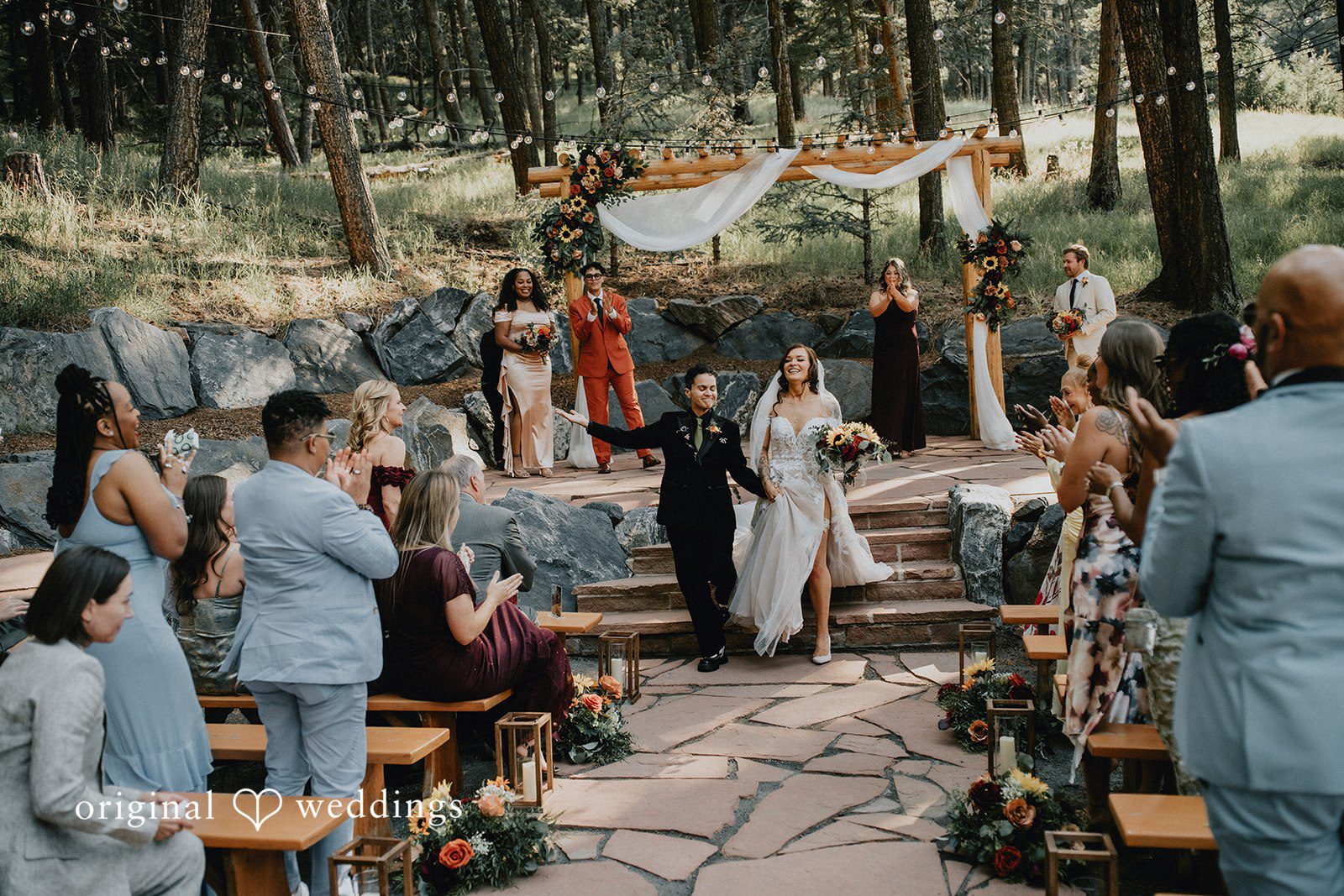 Jennifer + Danielle A wedding ceremony takes place in front of seated guests in a forest.