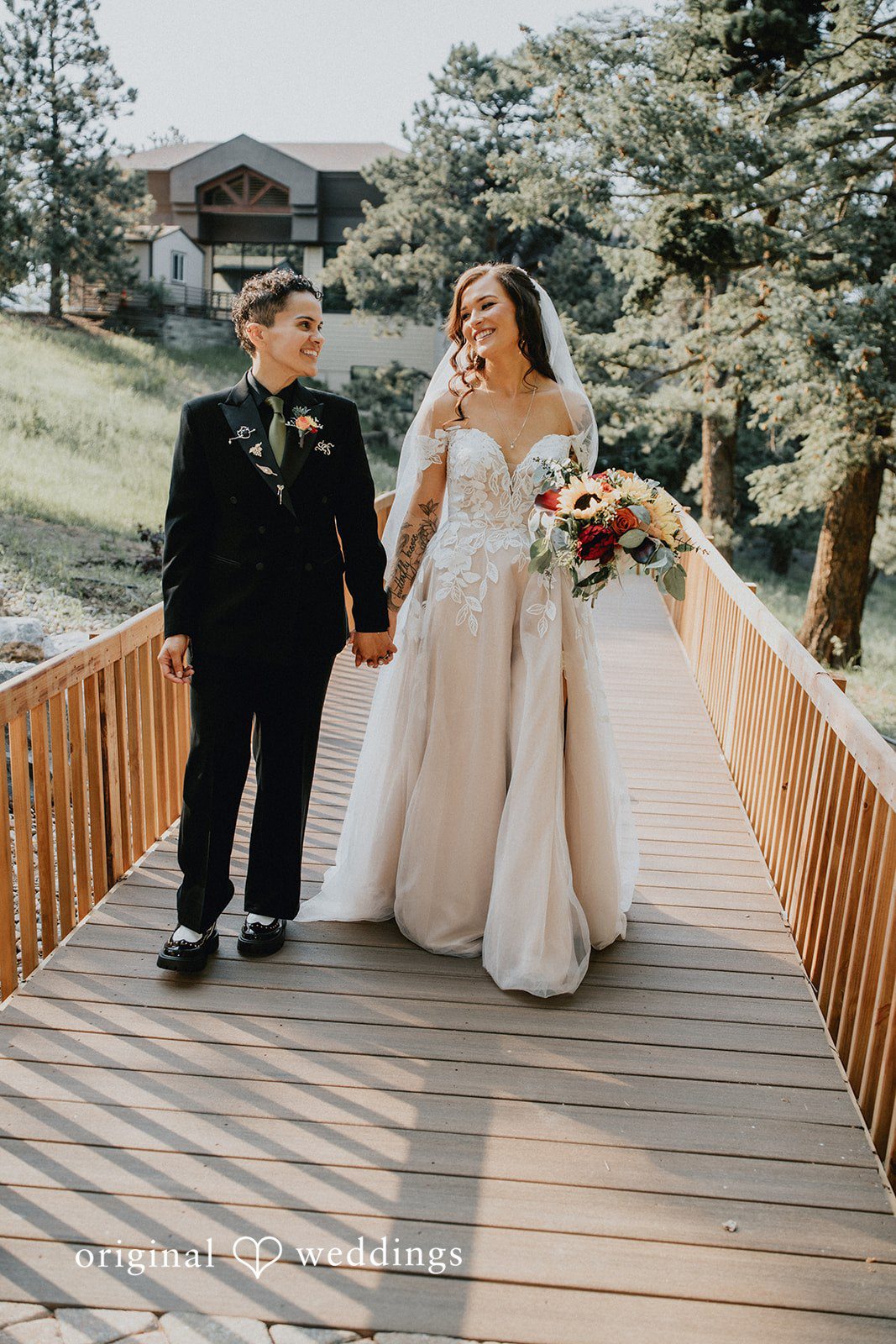 Jennifer + Danielle A couple walk hand-in-hand across a wooden bridge.