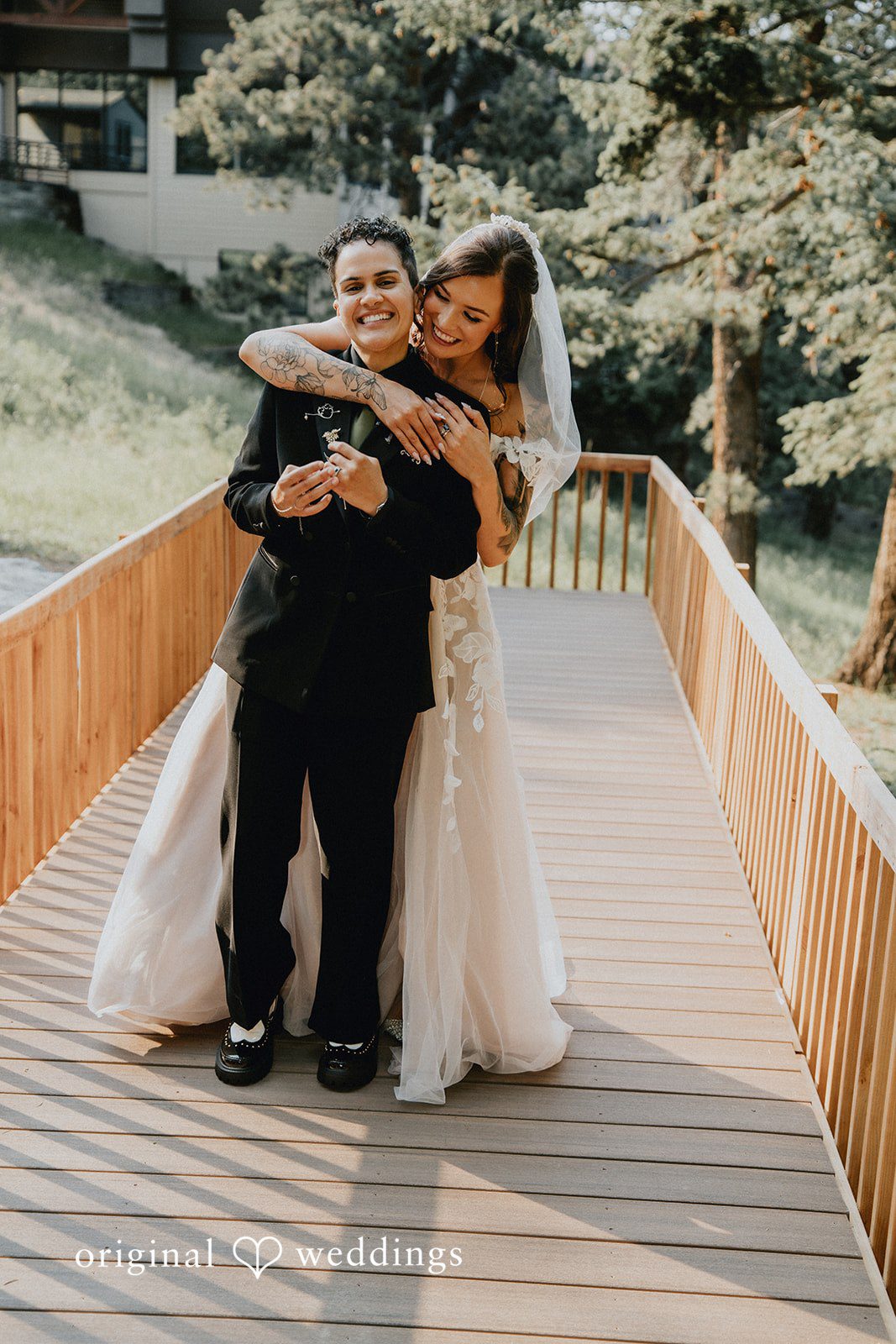 Jennifer + Danielle A groom lifts and holds the bride during a joyful moment on a wooden walkway.