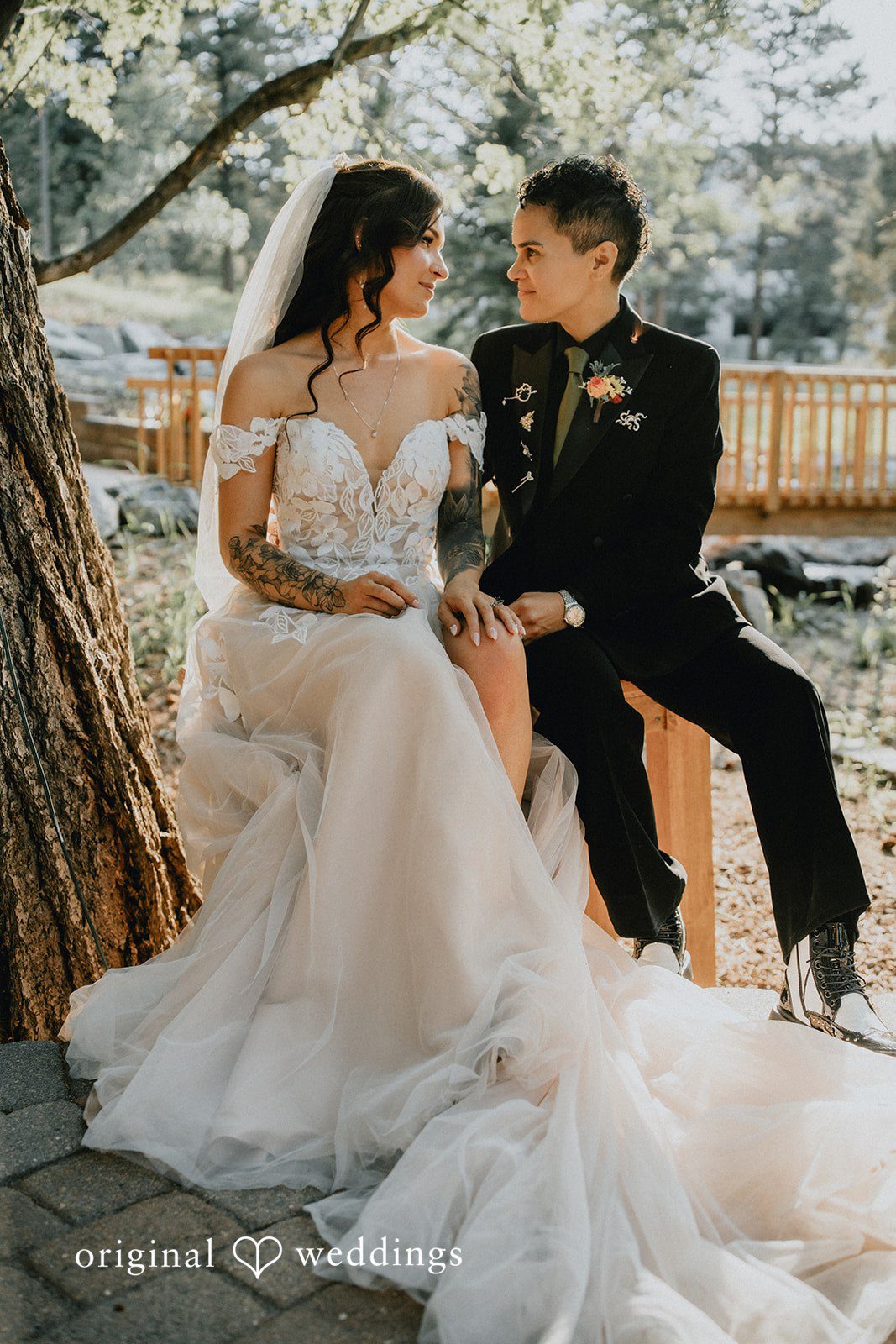 Jennifer + Danielle A bride in a layered gown sits next to the groom on a stone edge.