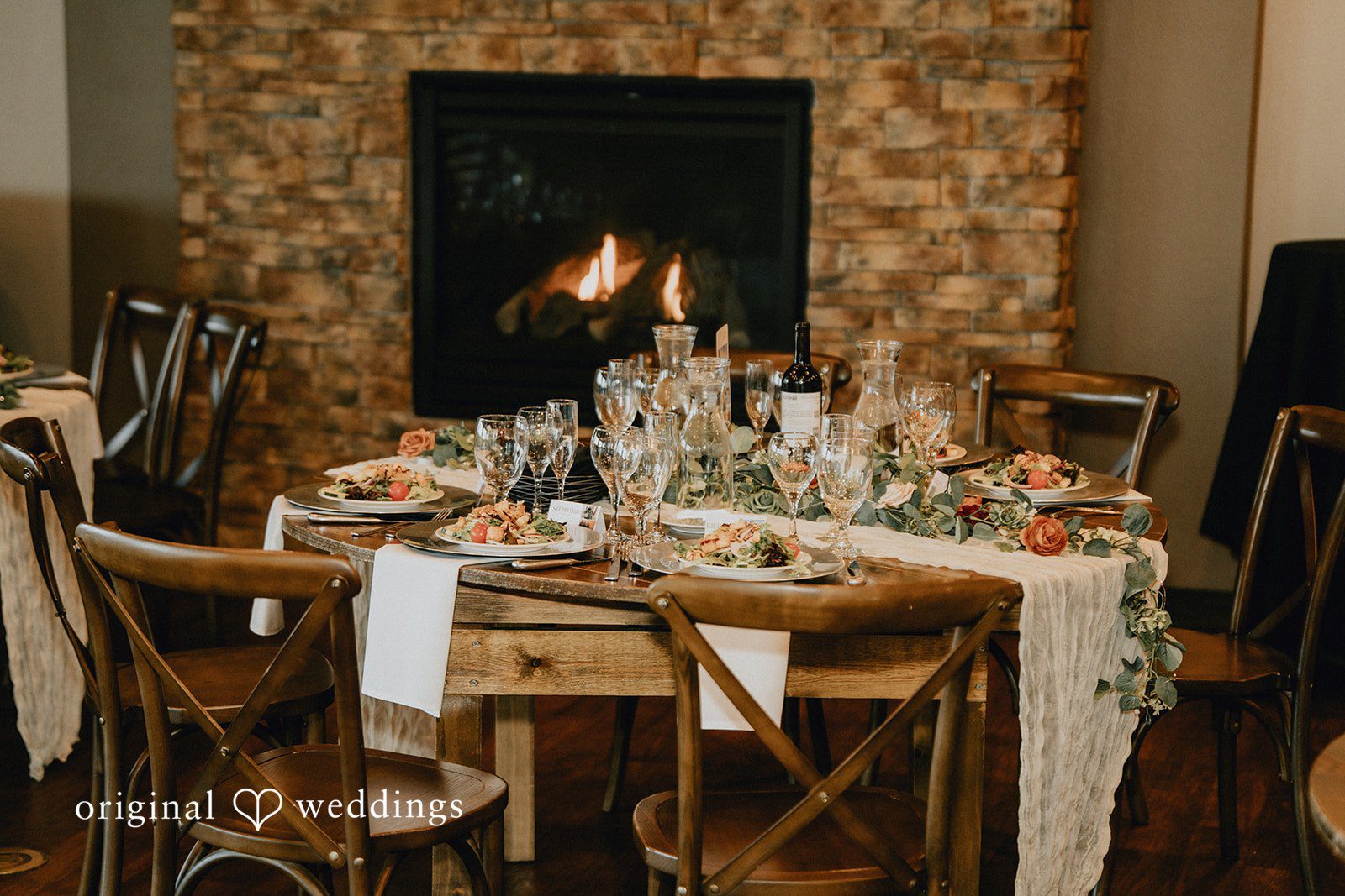 Jennifer + Danielle A rustic wooden dining table is fully set for a wedding reception.