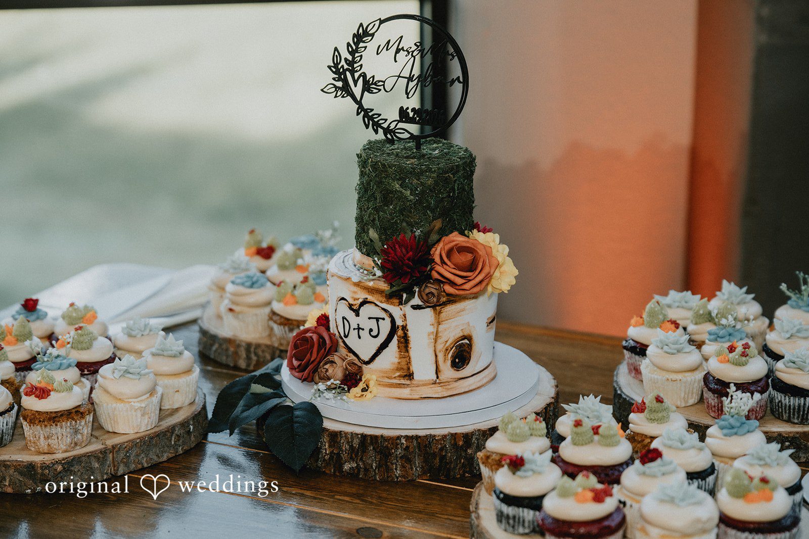 Jennifer + Danielle A multi-tiered wedding cake is displayed next to matching cupcakes on a table.