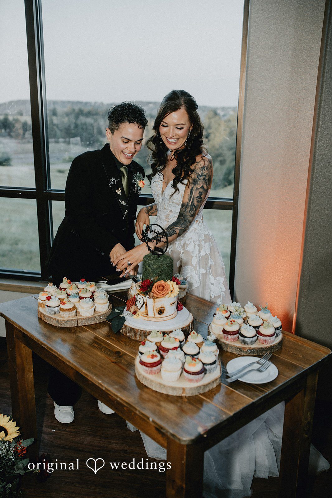 Jennifer + Danielle A couple cuts their wedding cake together at a dessert table.