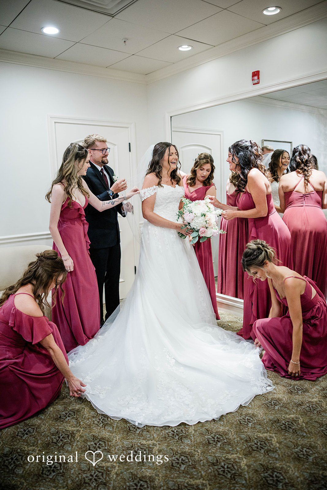 A bride surrounded by her bridesmaids in dark pink dresses.