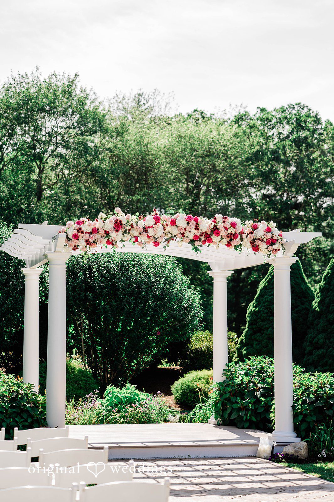 A white wedding altar decorated with vibrant pink floral arrangements.