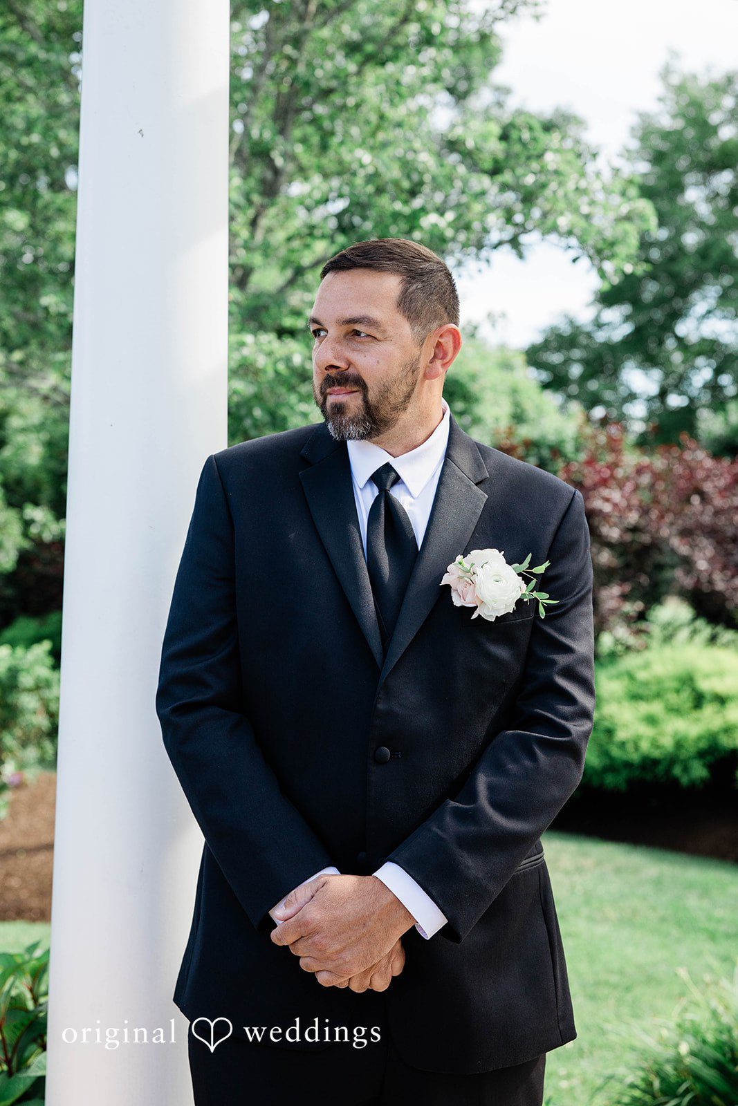 A groom smiling while standing next to a white column.