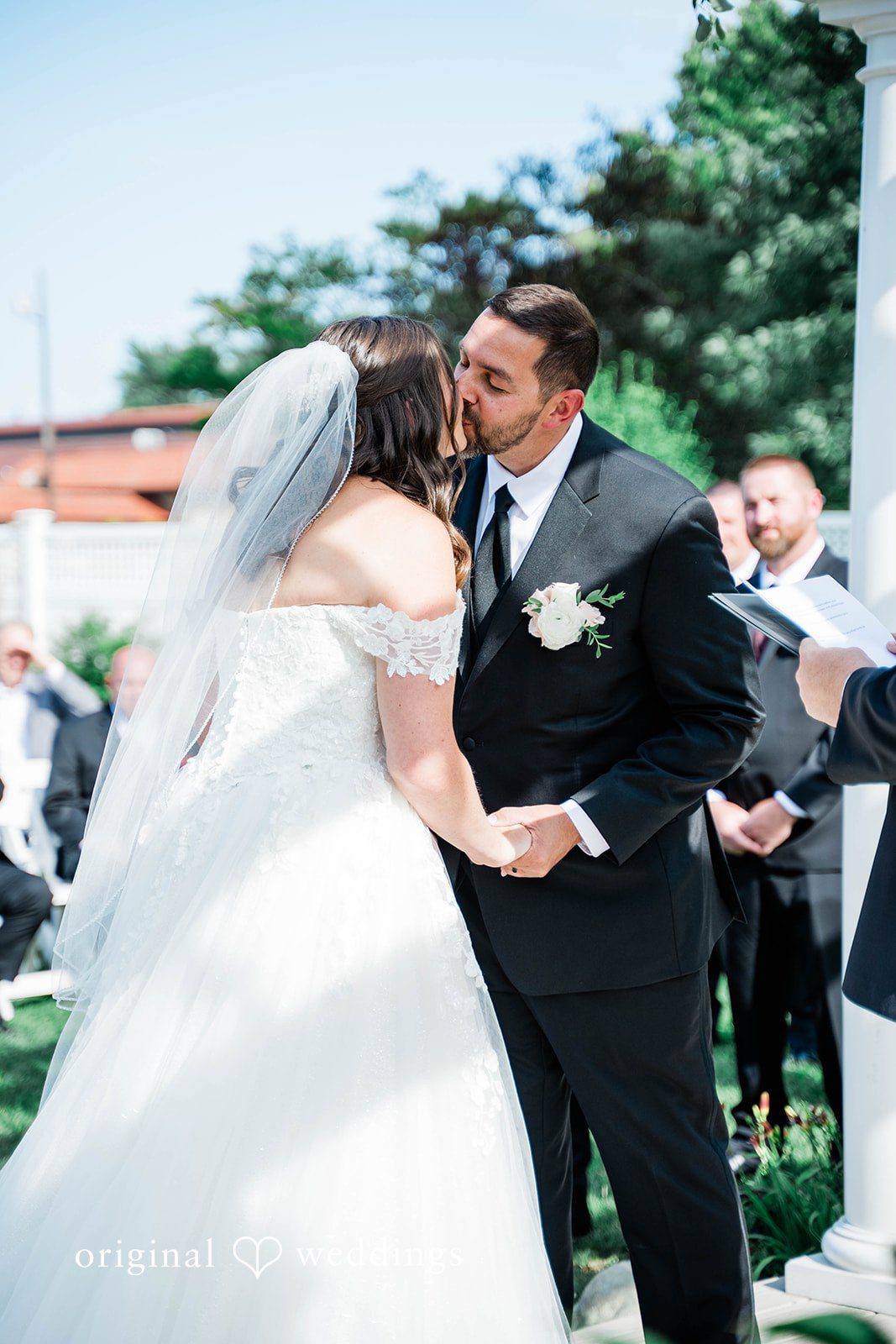 A bride and groom share a kiss while holding hands during their wedding ceremony.