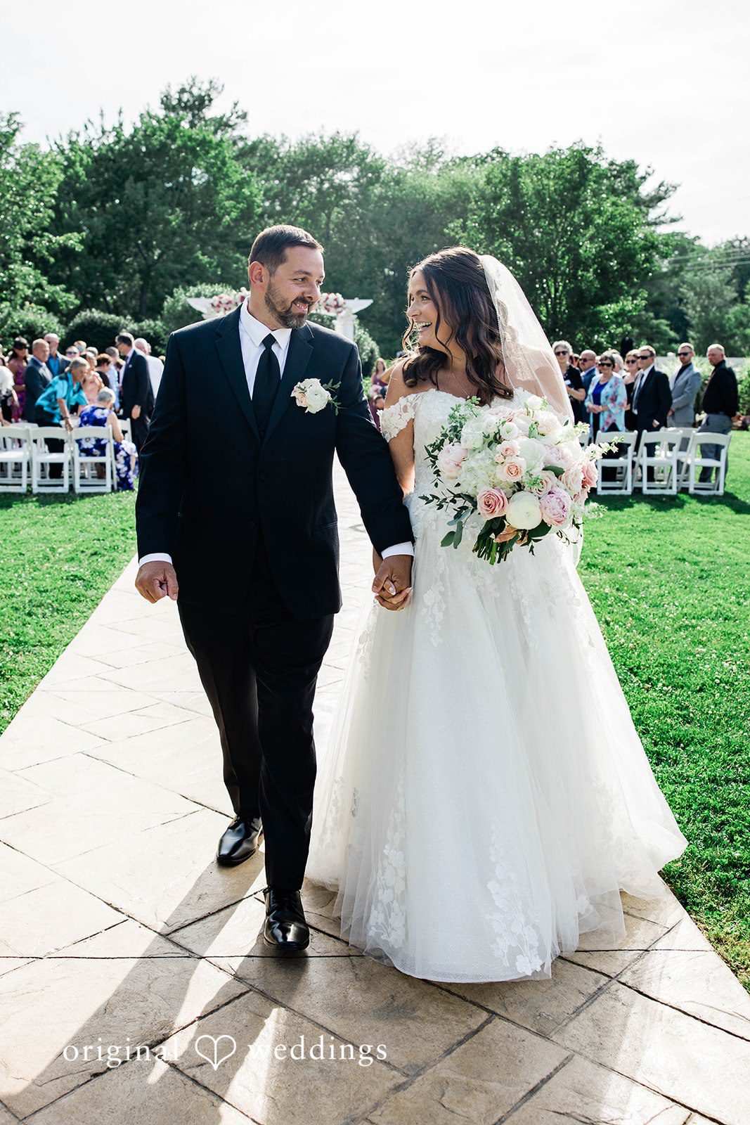 A newly married couple walking hand-in-hand down a pathway.