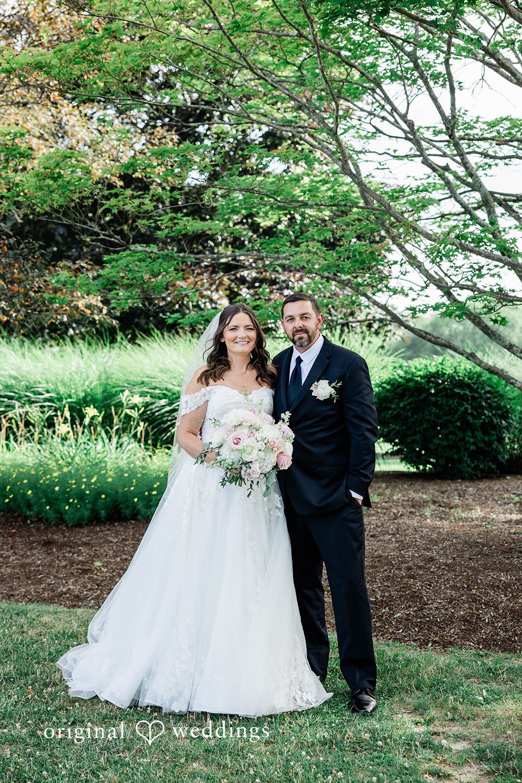 A bride and groom standing together in a grassy field.