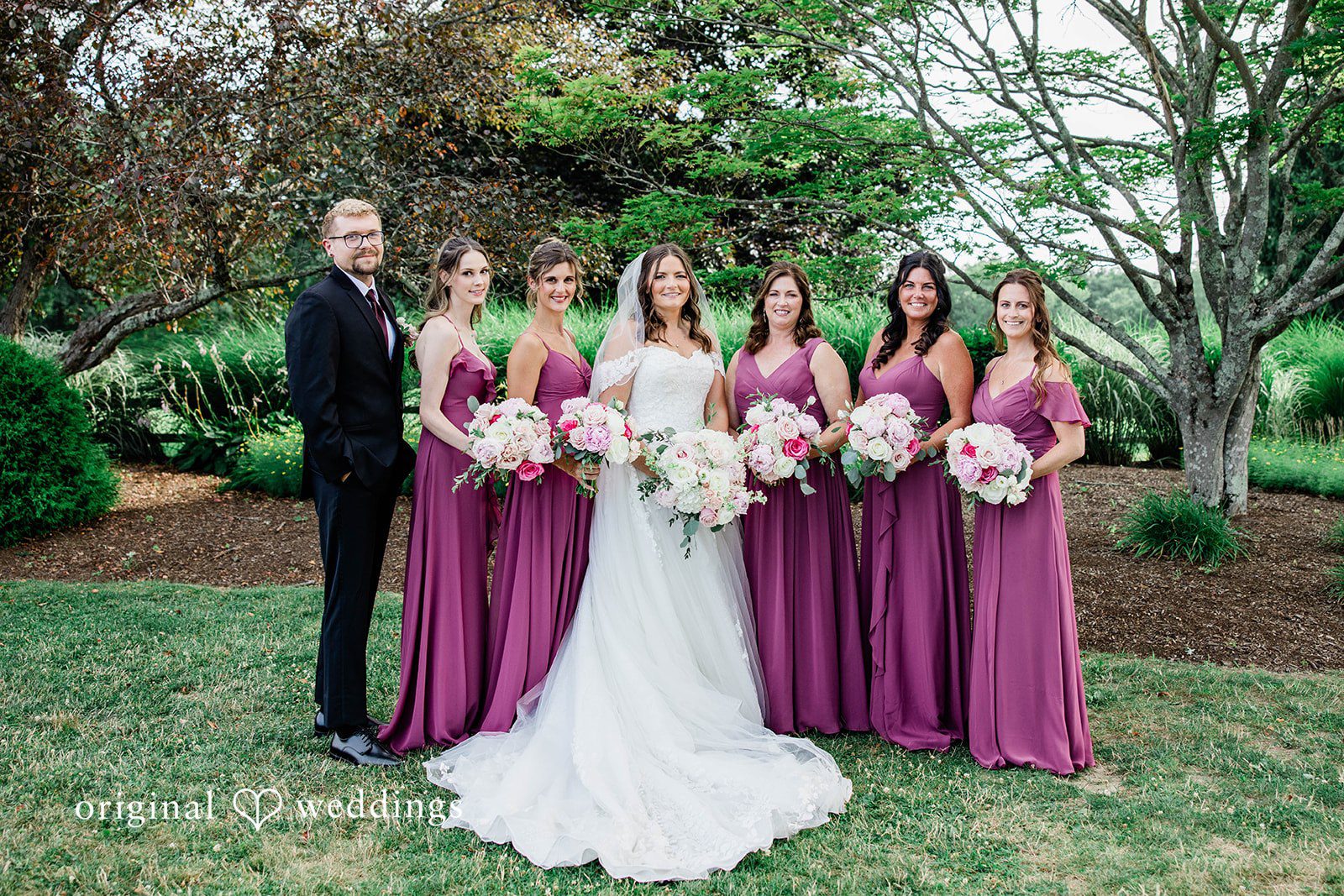 A bridal party in pink dresses holding bouquets and posing in a row.