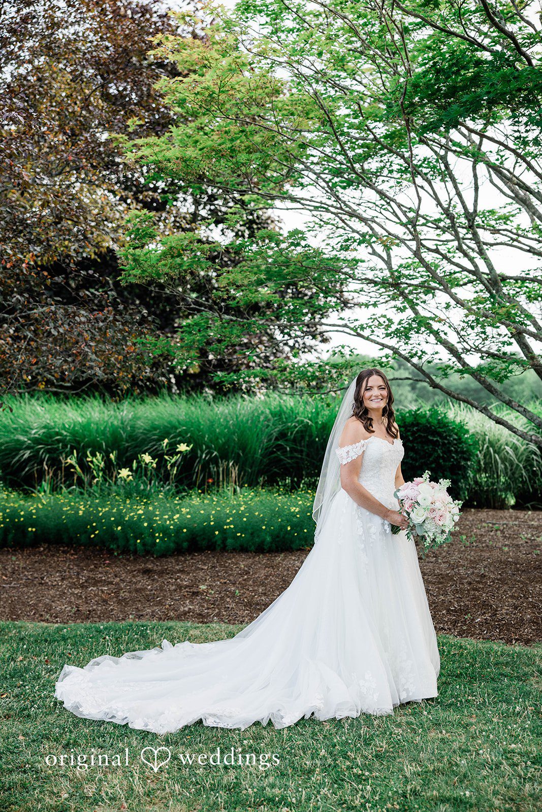 A bride in a long white gown posing on a green lawn.