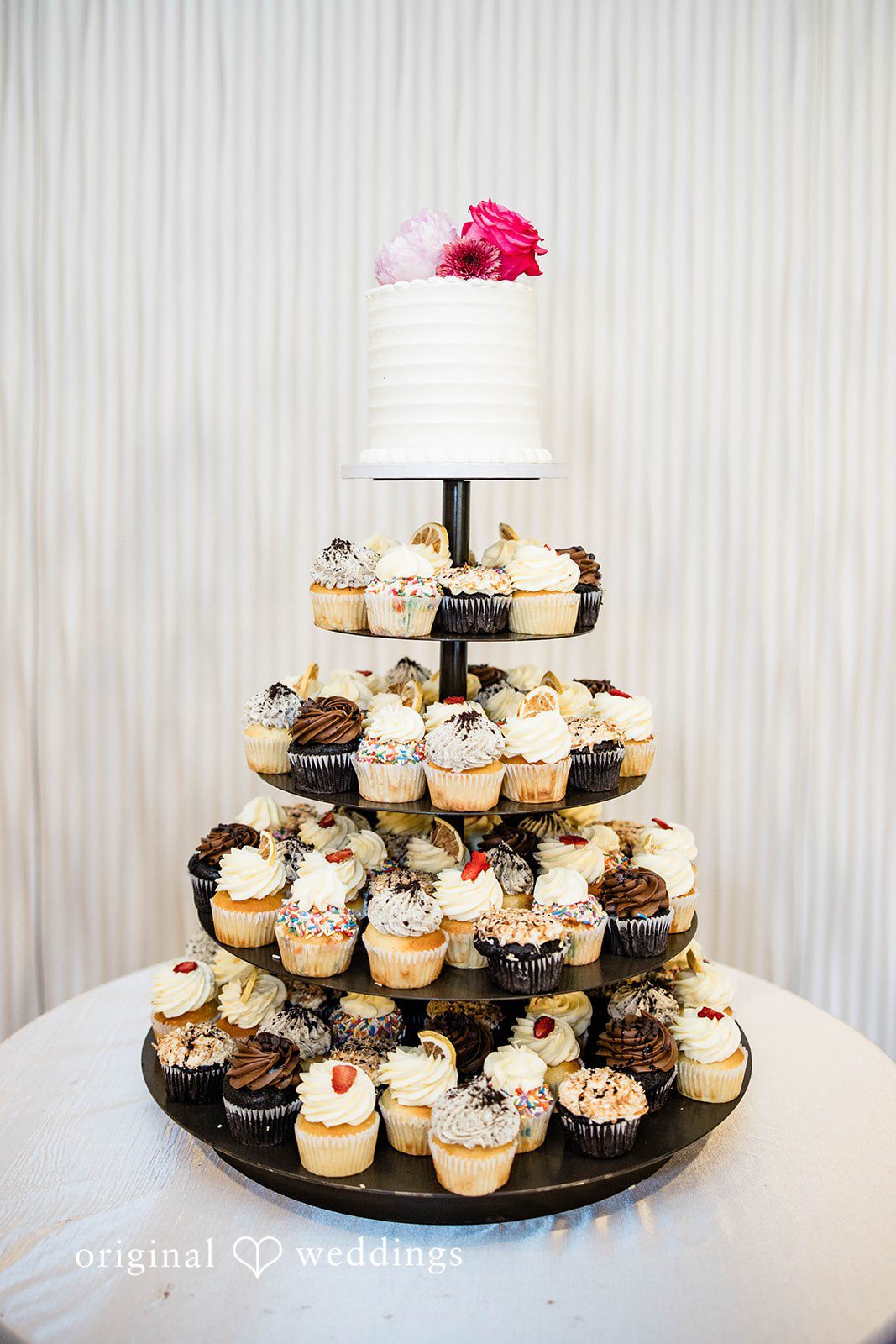 A multi-tiered wedding cupcake tower topped with a small cake.