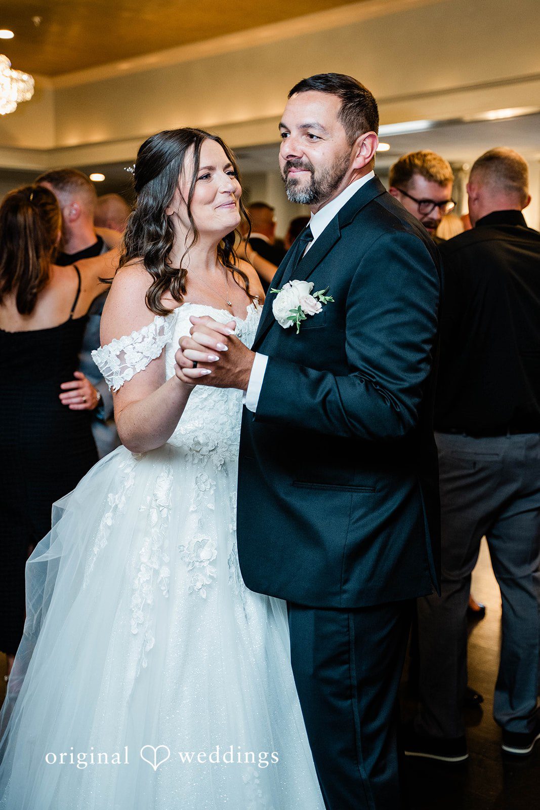 A bride and groom holding hands while slow dancing together.