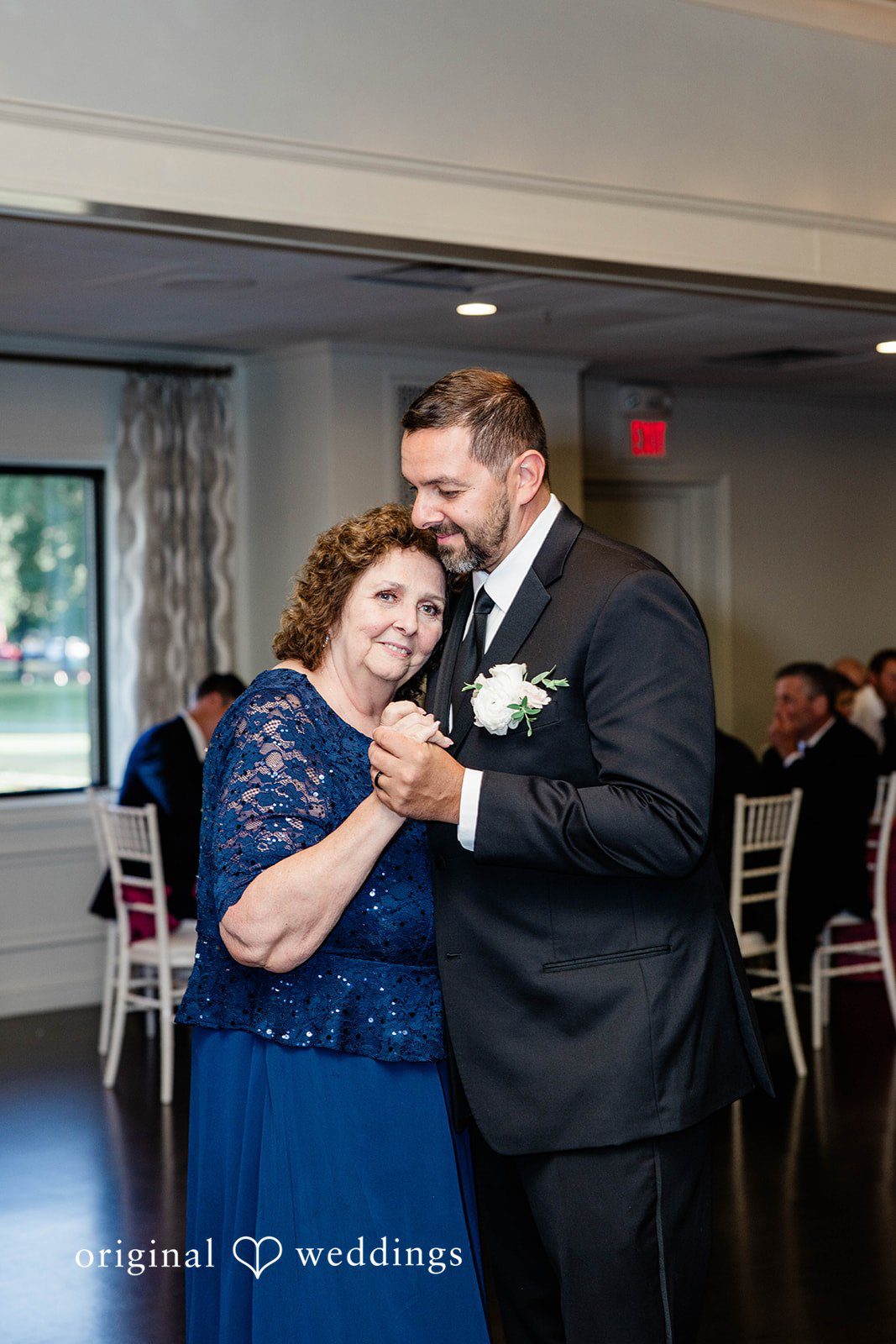 A groom in a suit dancing with a woman in a blue dress.