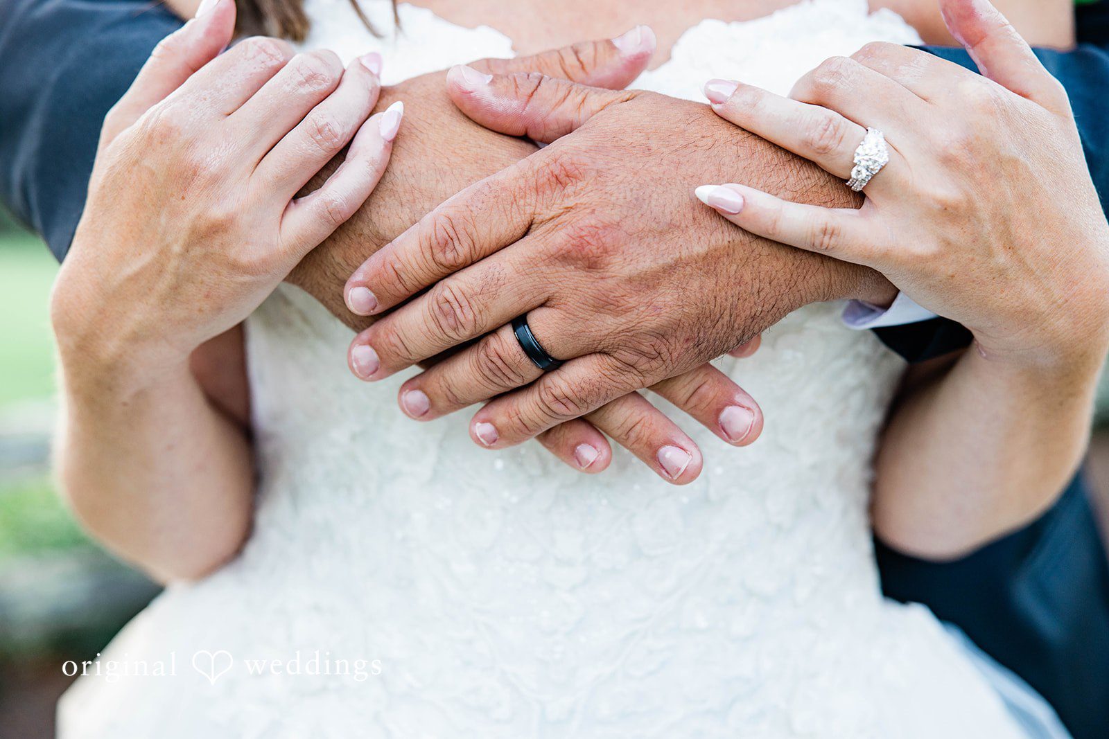 A close-up view of a bride and groom embracing, showing their wedding rings.