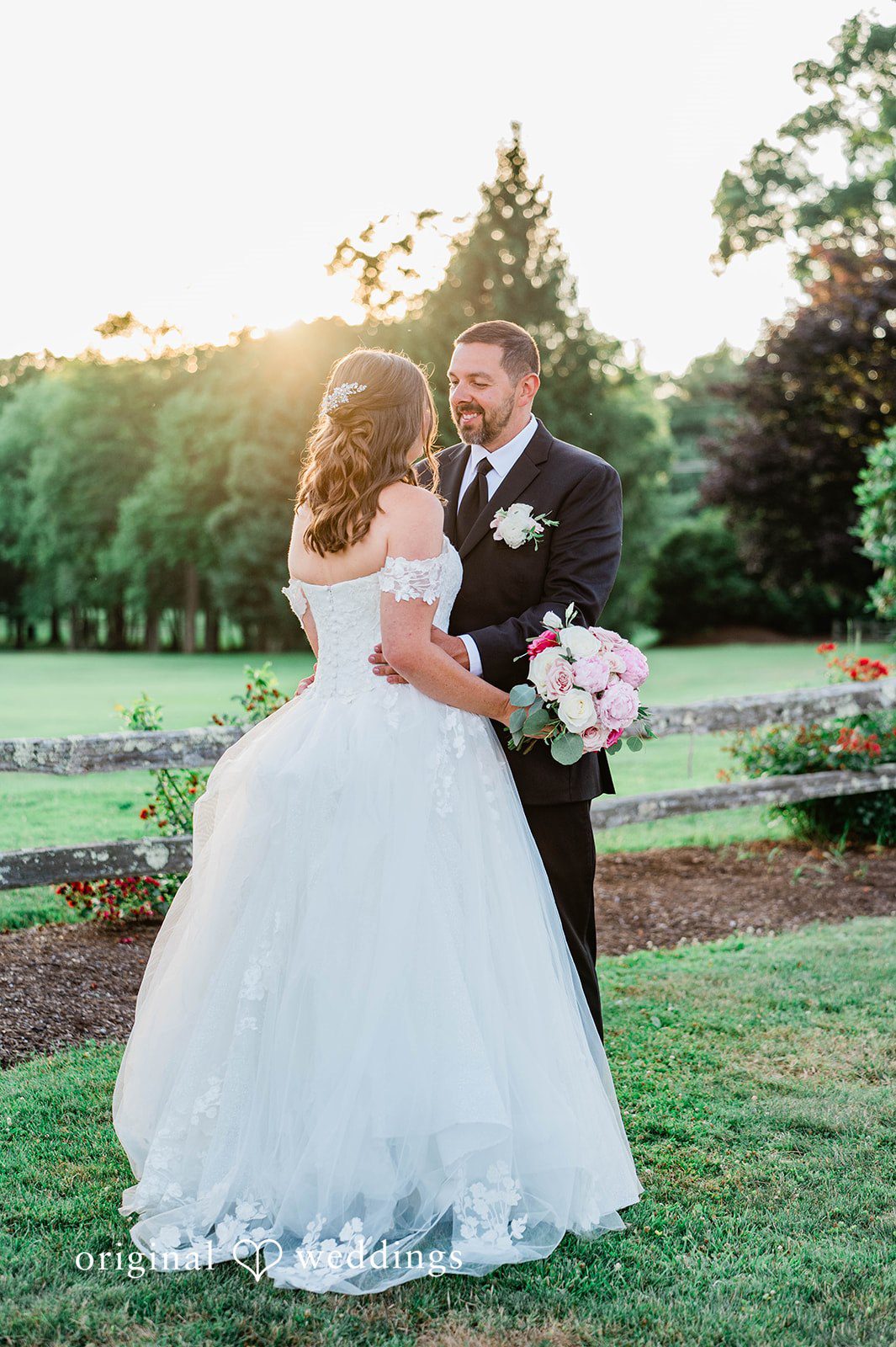 A bride and groom posing together at sunset on a lawn.
