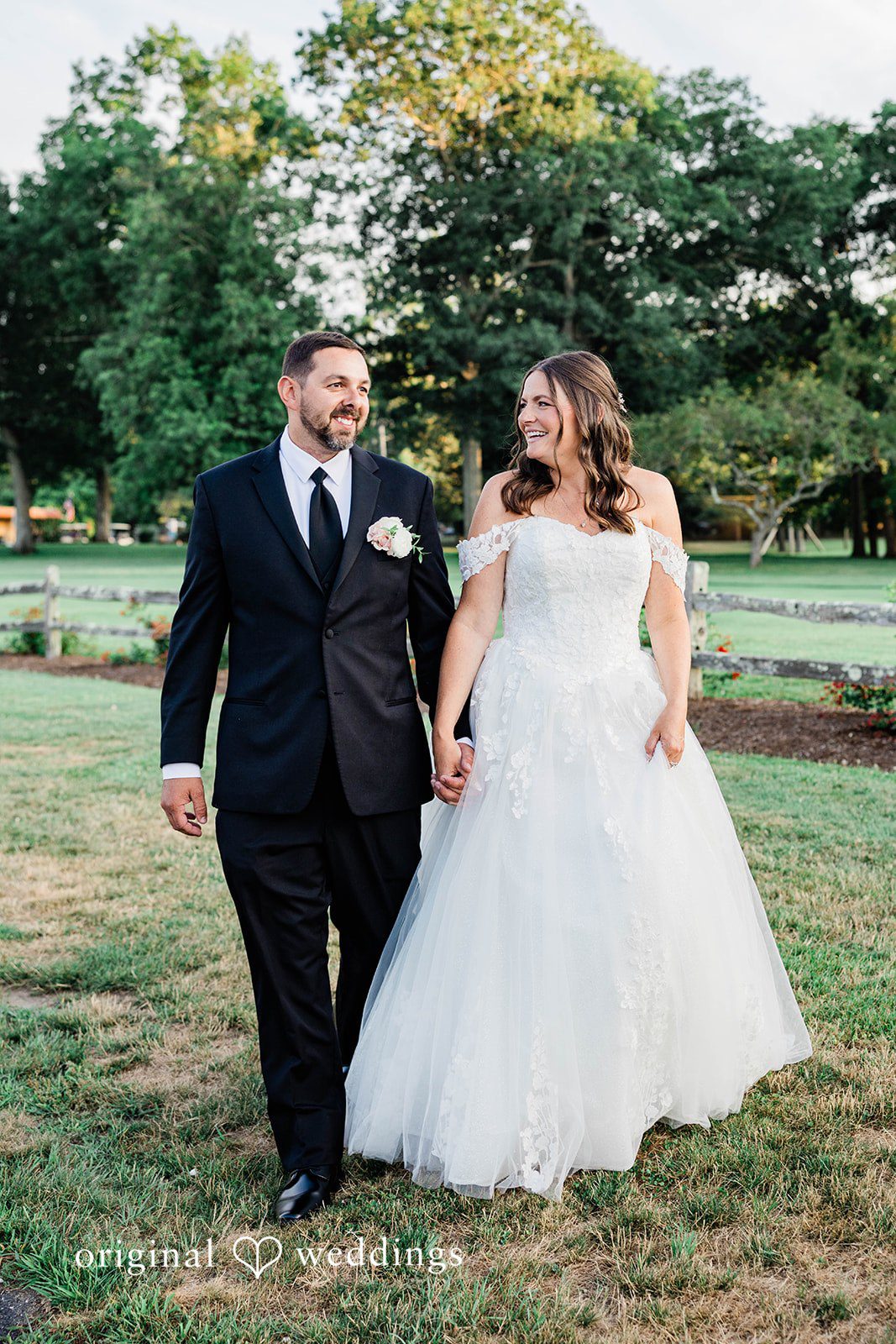 A bride and groom walking together and smiling on a grassy lawn.