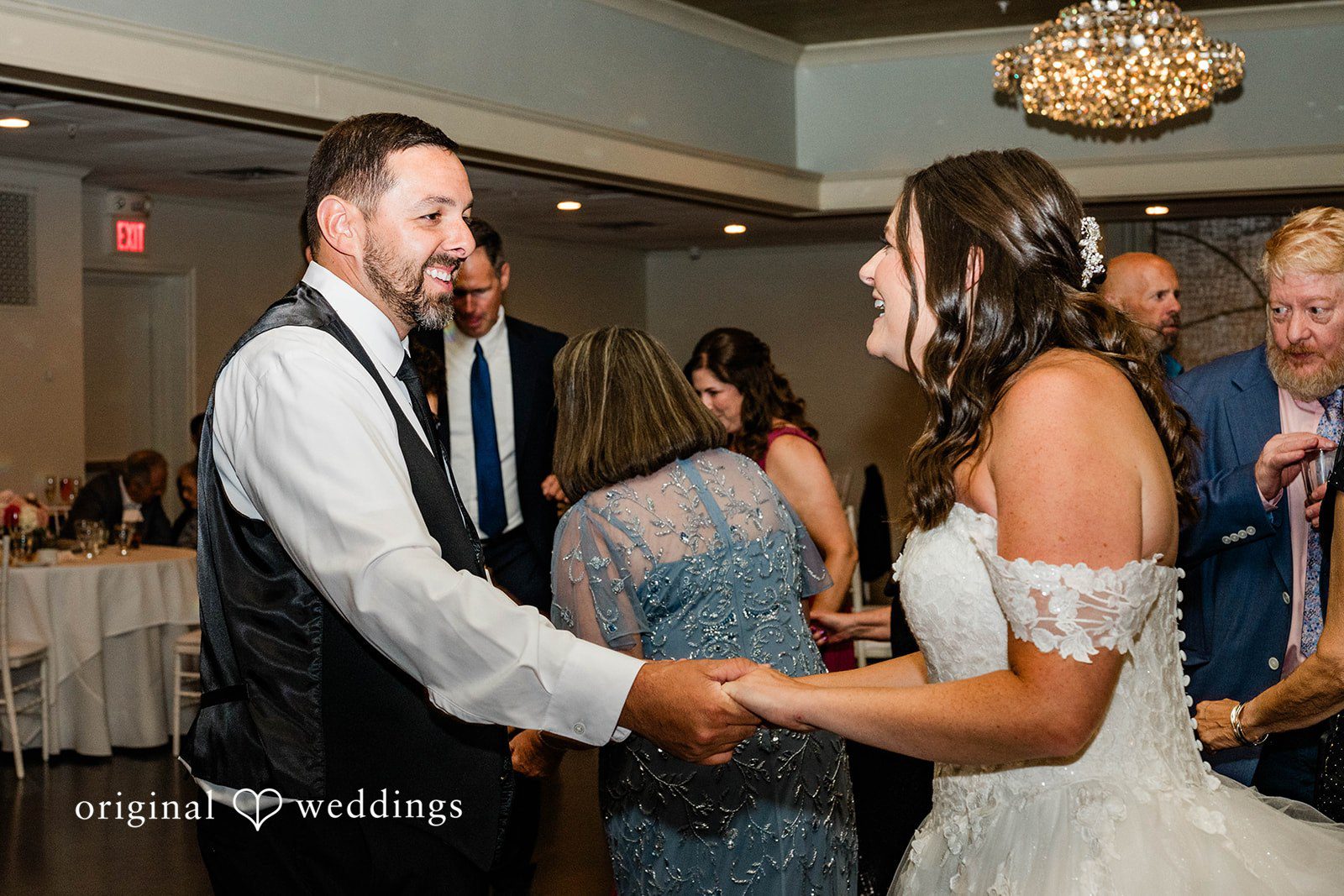 A bride and groom holding hands while smiling at each other on the dance floor.