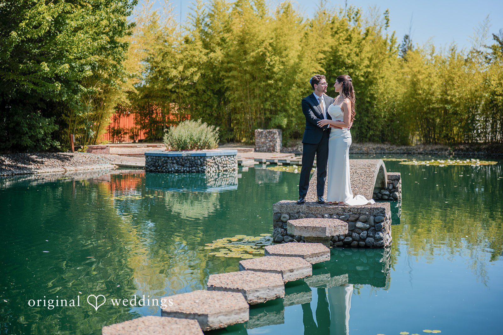 Zechariah + Tova A couple posing together on an arched stone bridge surrounded by lush green trees.