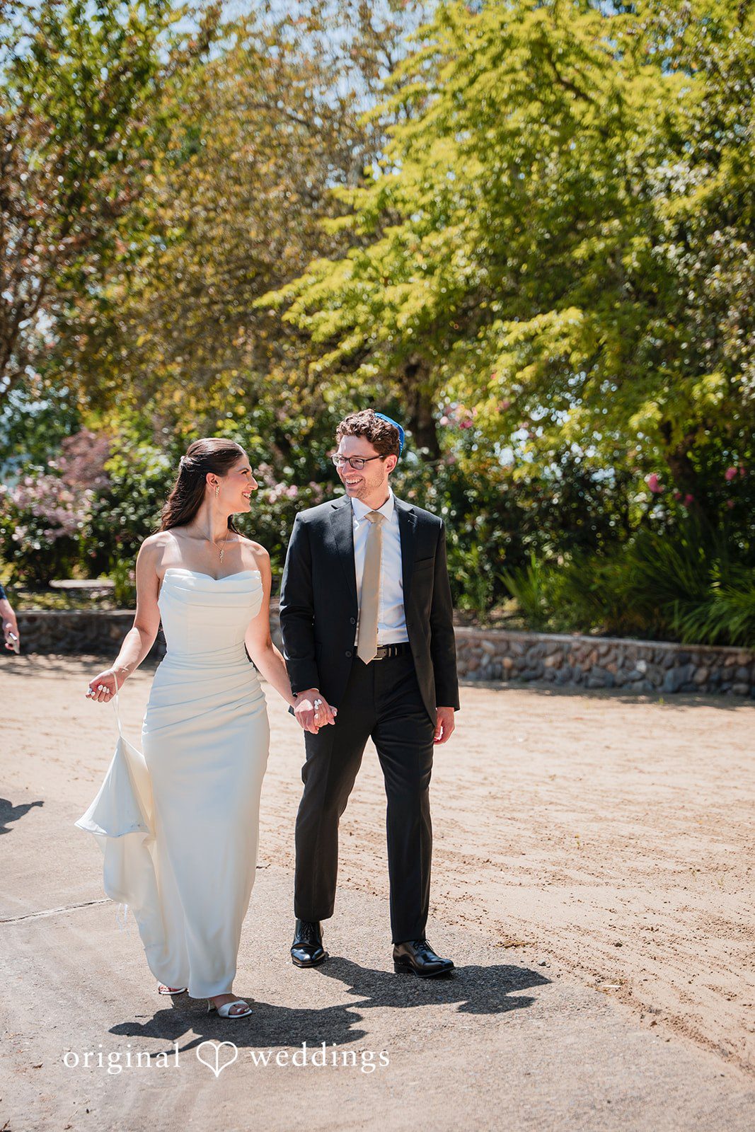 Zechariah + Tova A bride and groom holding hands and walking across stepping stones over a pool of water.