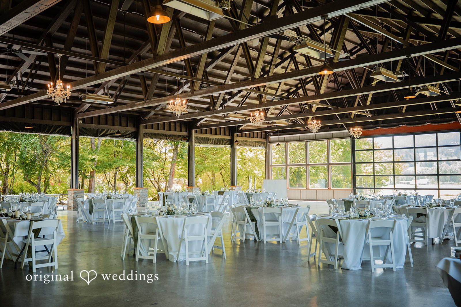 Zechariah + Tova A wedding reception hall filled with white dining tables and chairs under a high wooden ceiling structure.