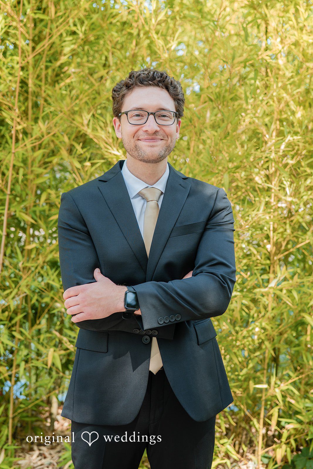 Zechariah + Tova A groom wearing a dark suit and glasses standing against a background of green bamboo stalks.