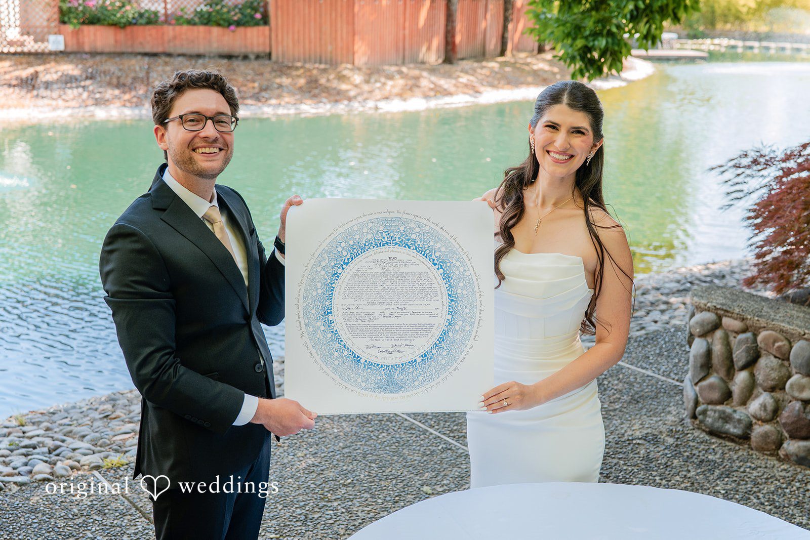 Zechariah + Tova A bride and groom holding a framed, decorative document between them.