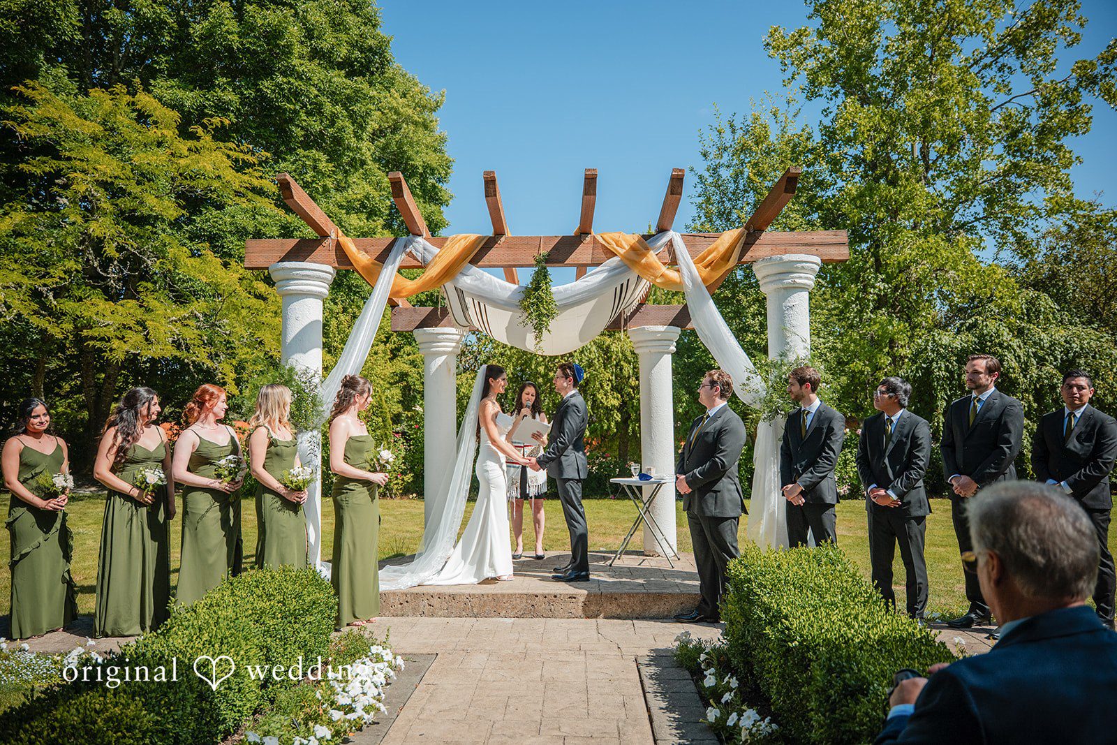 Zechariah + Tova A wide view of a wedding ceremony under a decorated chuppah structure surrounded by guests.