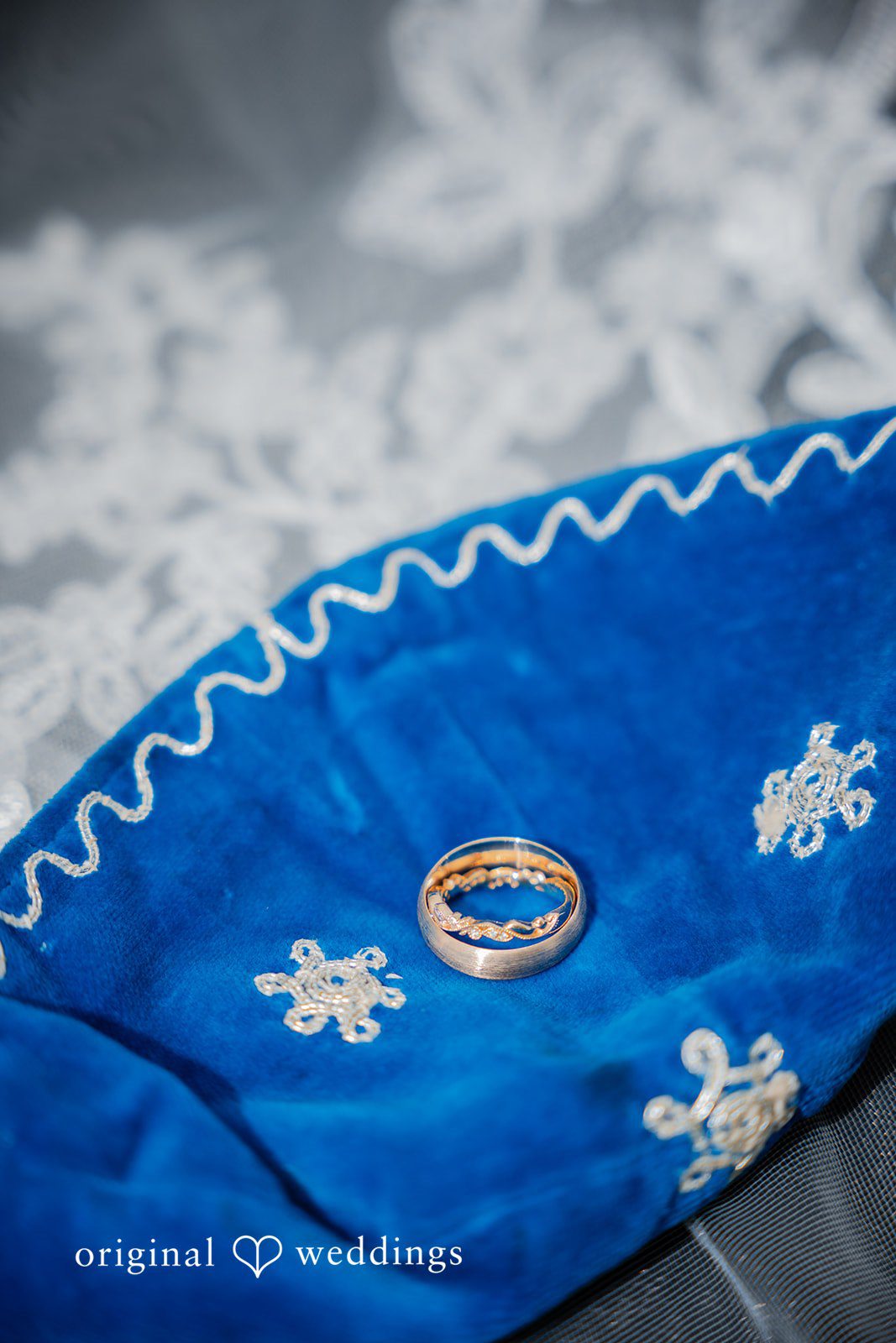 Zechariah + Tova A close-up of a blue fabric item featuring two metallic gold wedding rings resting on top.