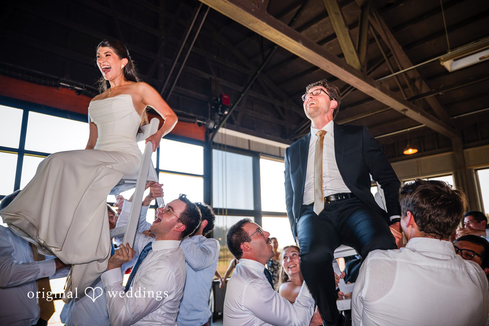 Zechariah + Tova A bride and groom being lifted on chairs by wedding guests.