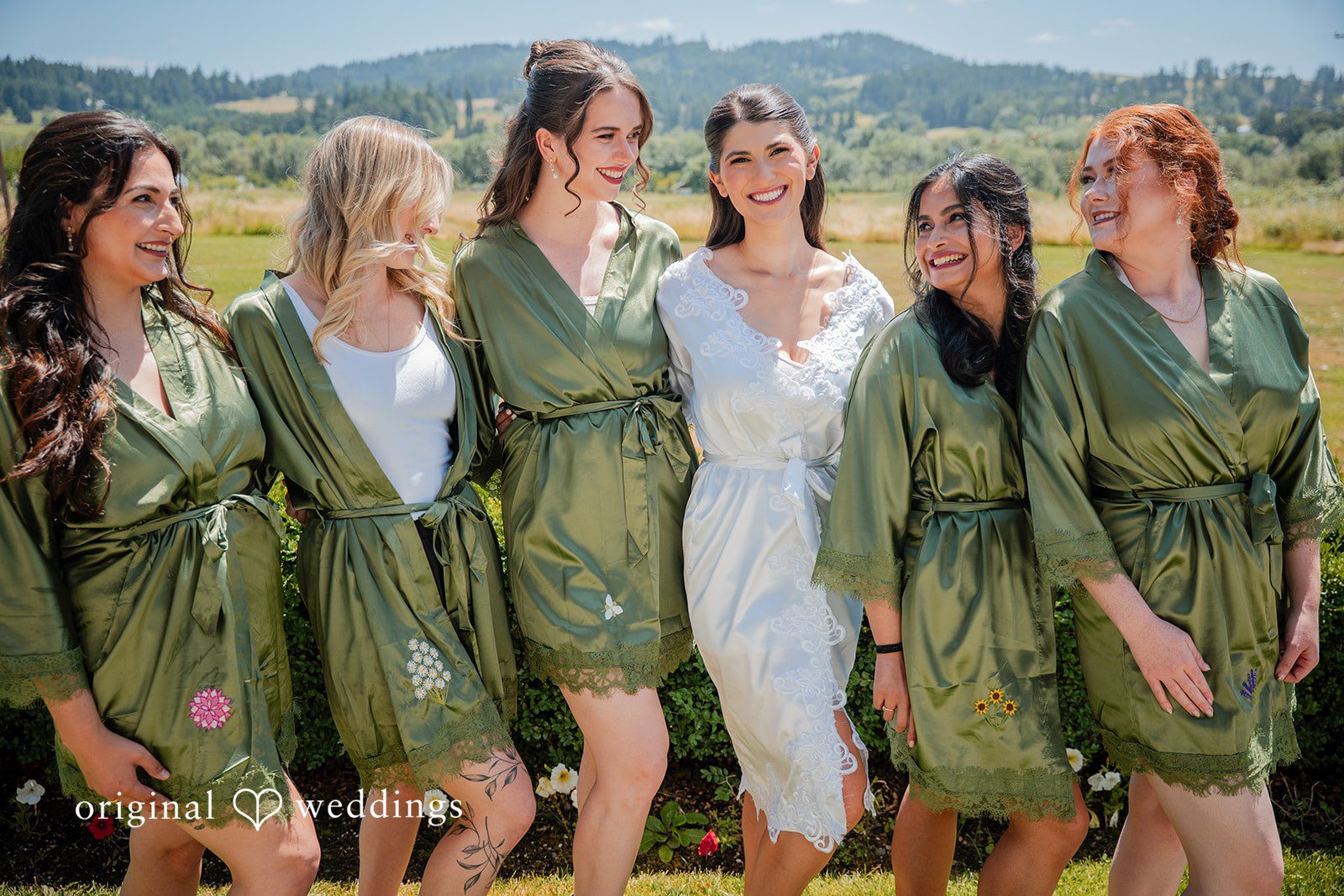 Zechariah + Tova Bride and Bridesmaid wearing matching green floral robes posing together in a line.